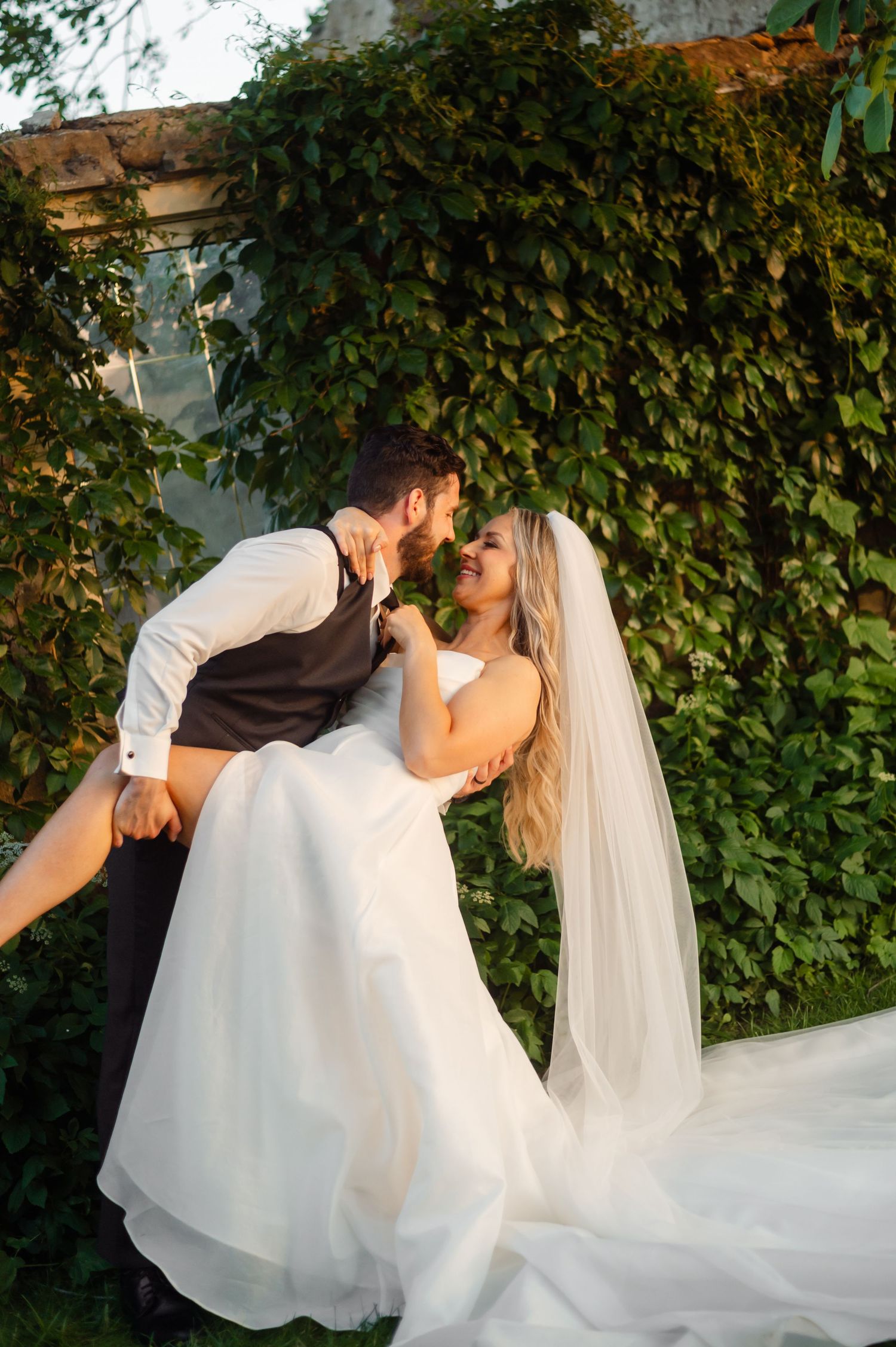 Romantic wedding couple shares intimate moments against a wall of green ivy.