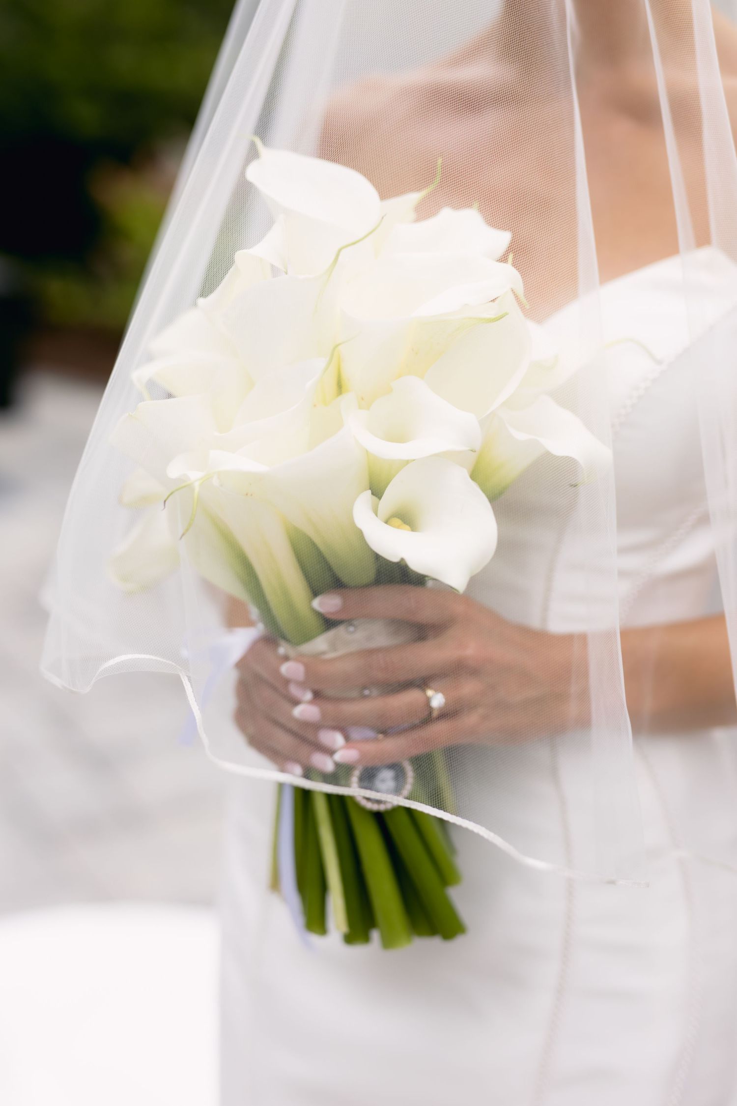 Bride holding elegant white calla lily bouquet with diamond engagement ring visible on hand.