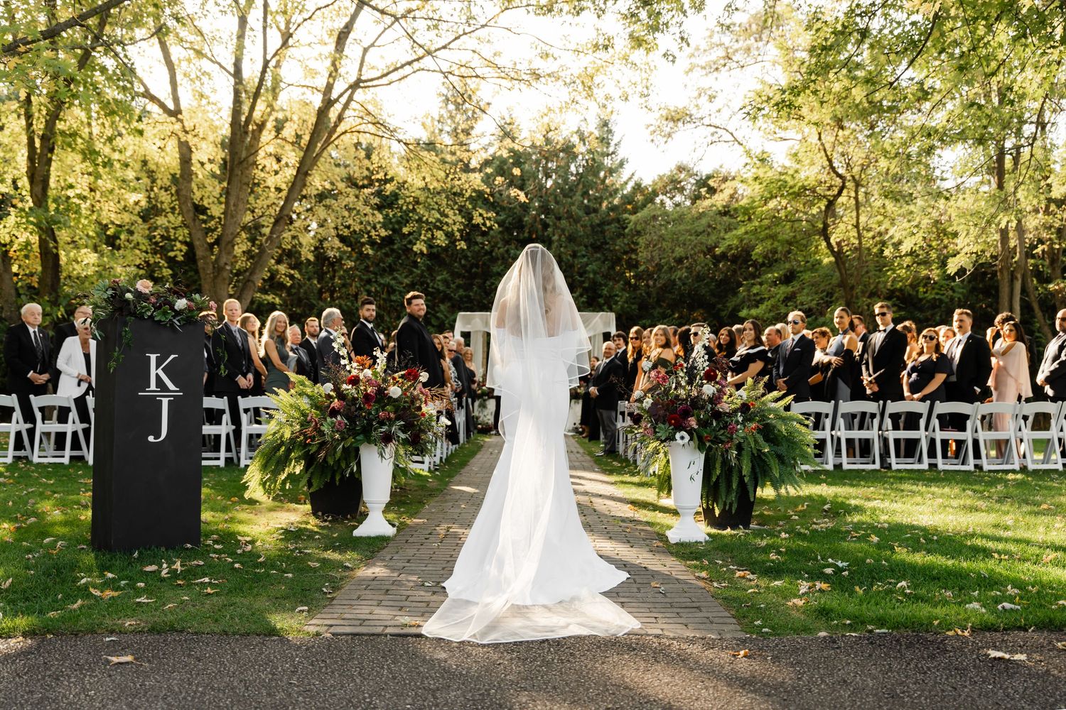 Wedding ceremony exit along stone pathway surrounded by autumn trees and white chairs.