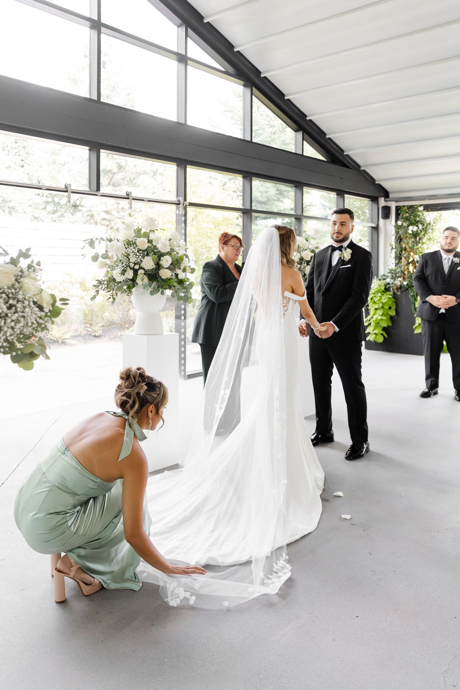 Bridesmaid in mint green dress adjusting wedding gown train on white floor.