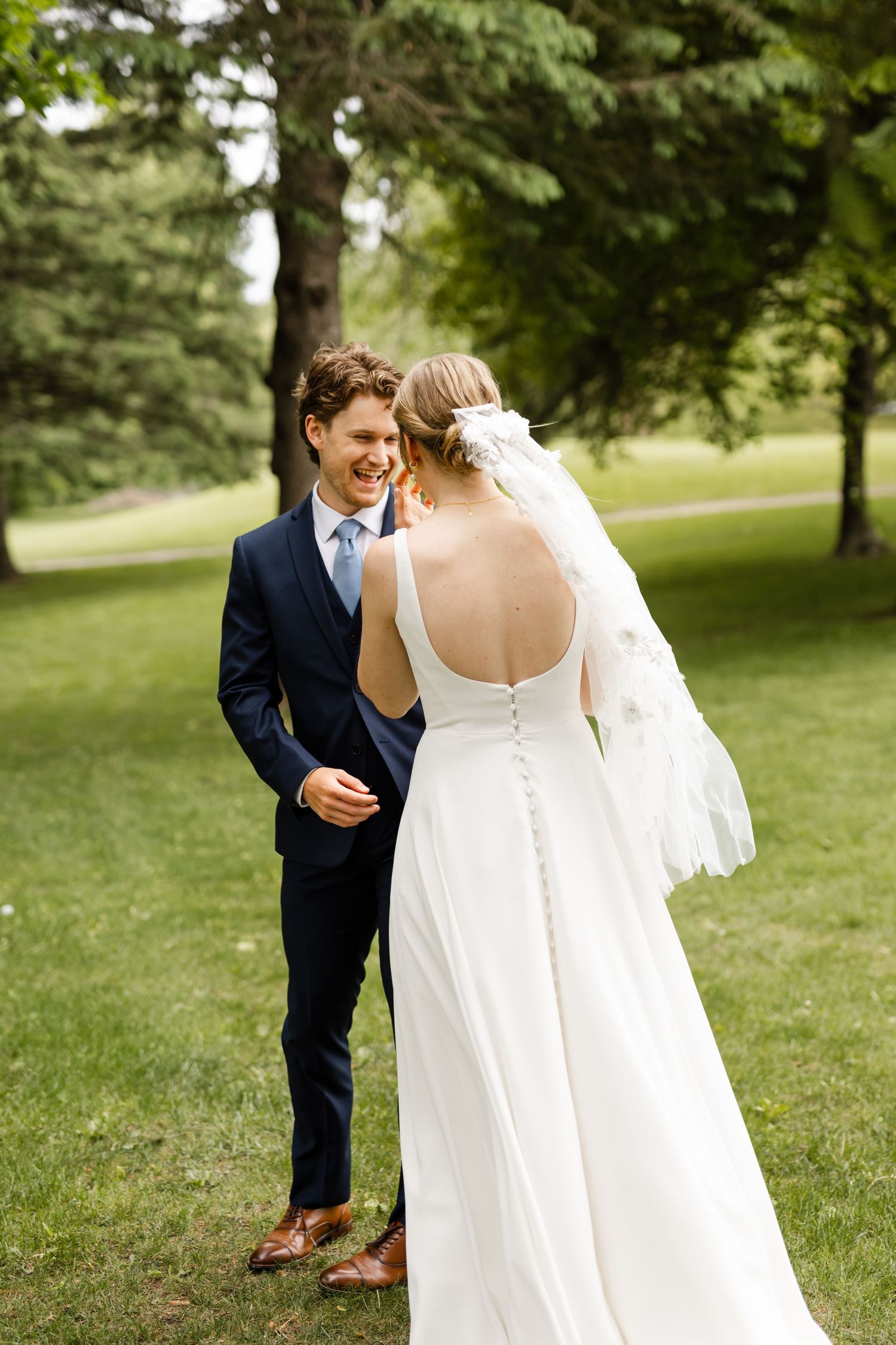 First look moment between couple in wedding attire under green trees.