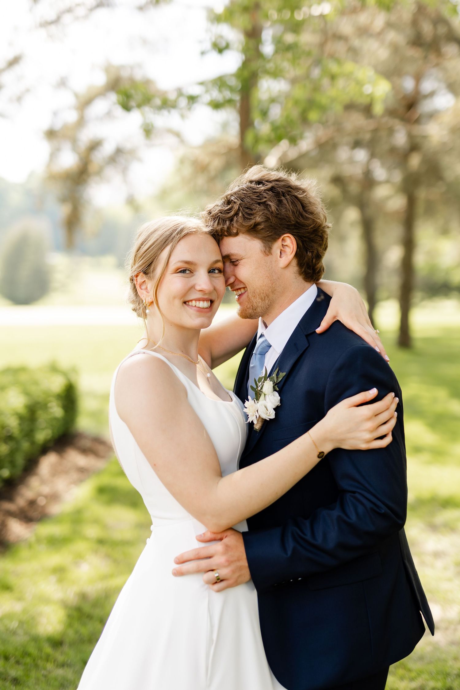 Joyful wedding couple embracing in sunlit garden setting.