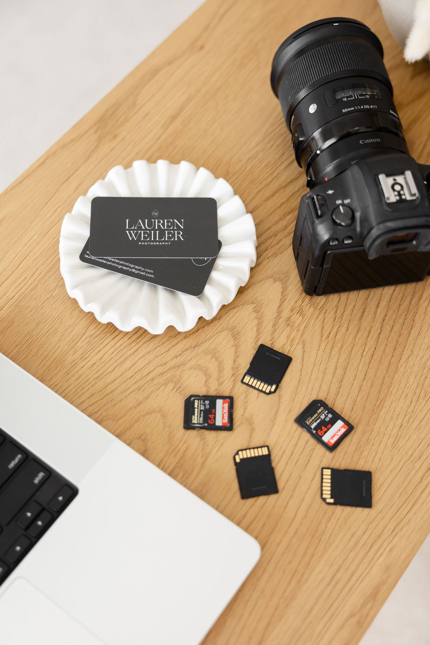 Photography equipment including memory cards, camera lens and business cards arranged on wooden desk.