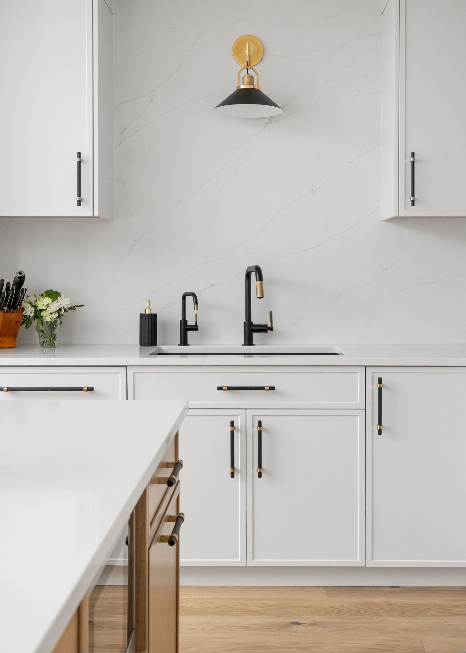 Clean white kitchen with black fixtures, marble backsplash, and wooden lower cabinets.