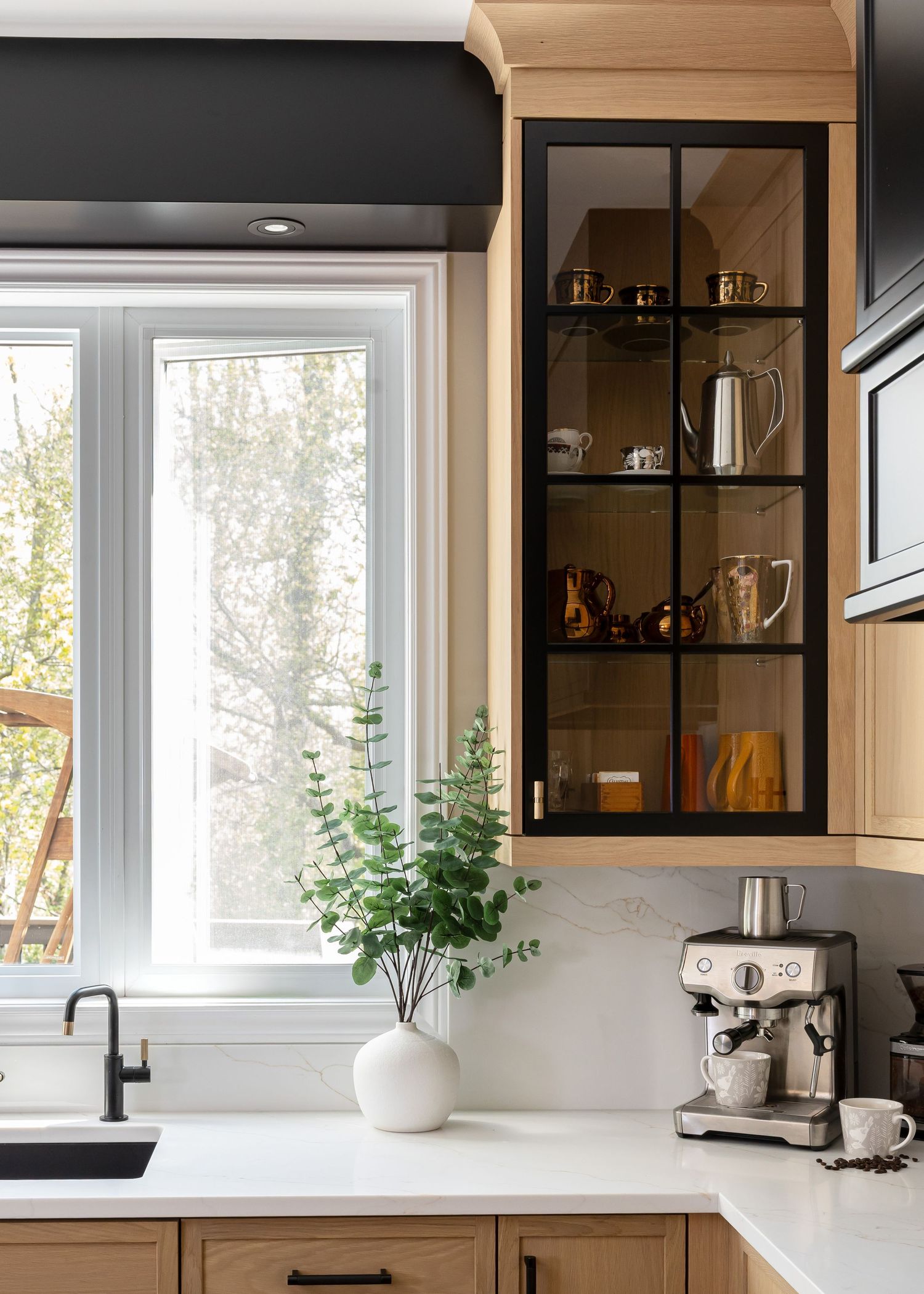 Bright kitchen with multiple windows, glass-front cabinets, and white countertops featuring modern appliances.