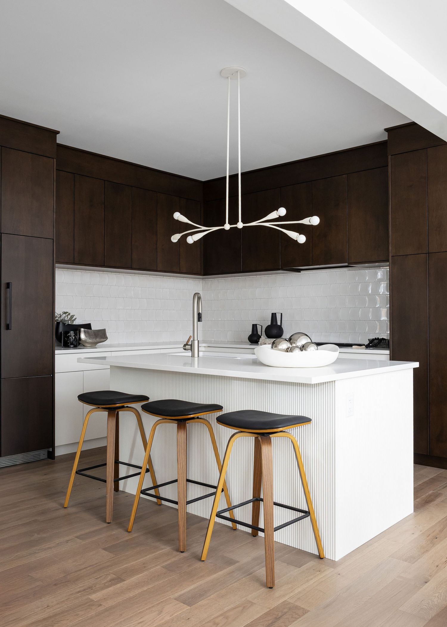 Minimalist kitchen featuring wooden bar stools, white island and dark wood cabinetry.