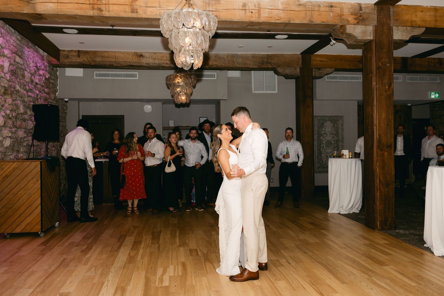 Wedding guests watch as dancers perform on a hardwood dance floor under crystal chandeliers.