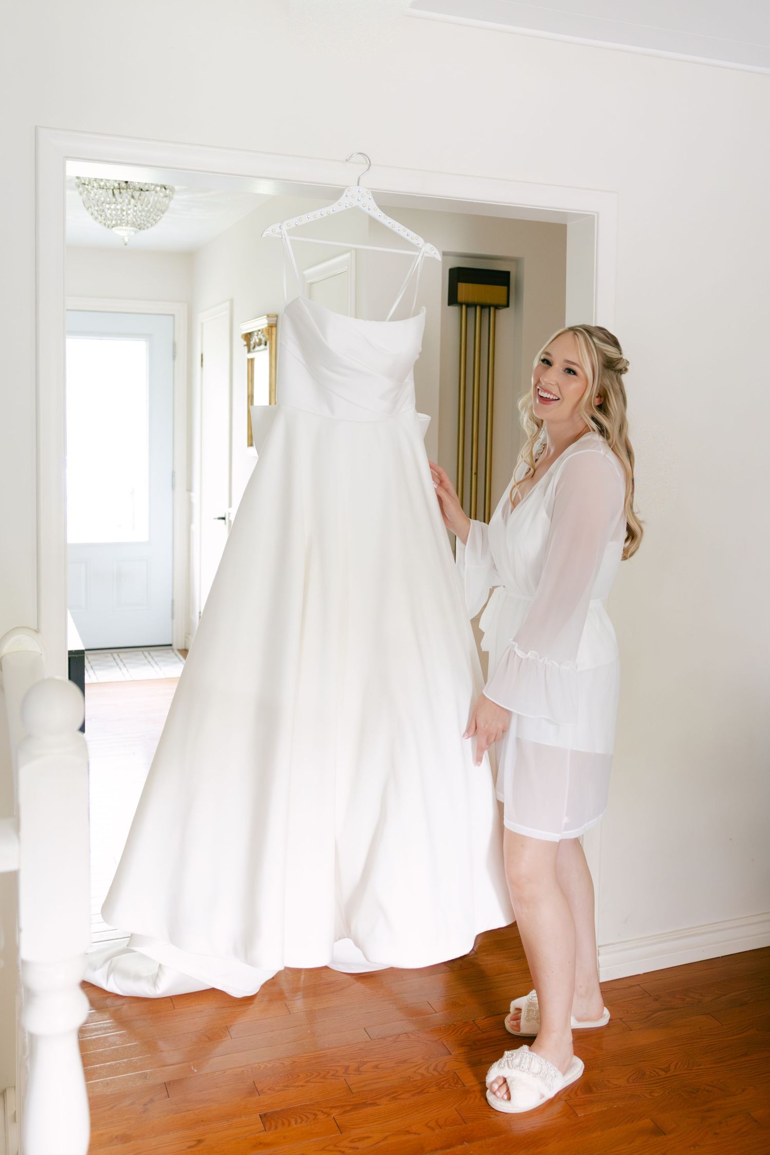 Wedding dress preparations with white gowns displayed on hangers in bright sunlit room.