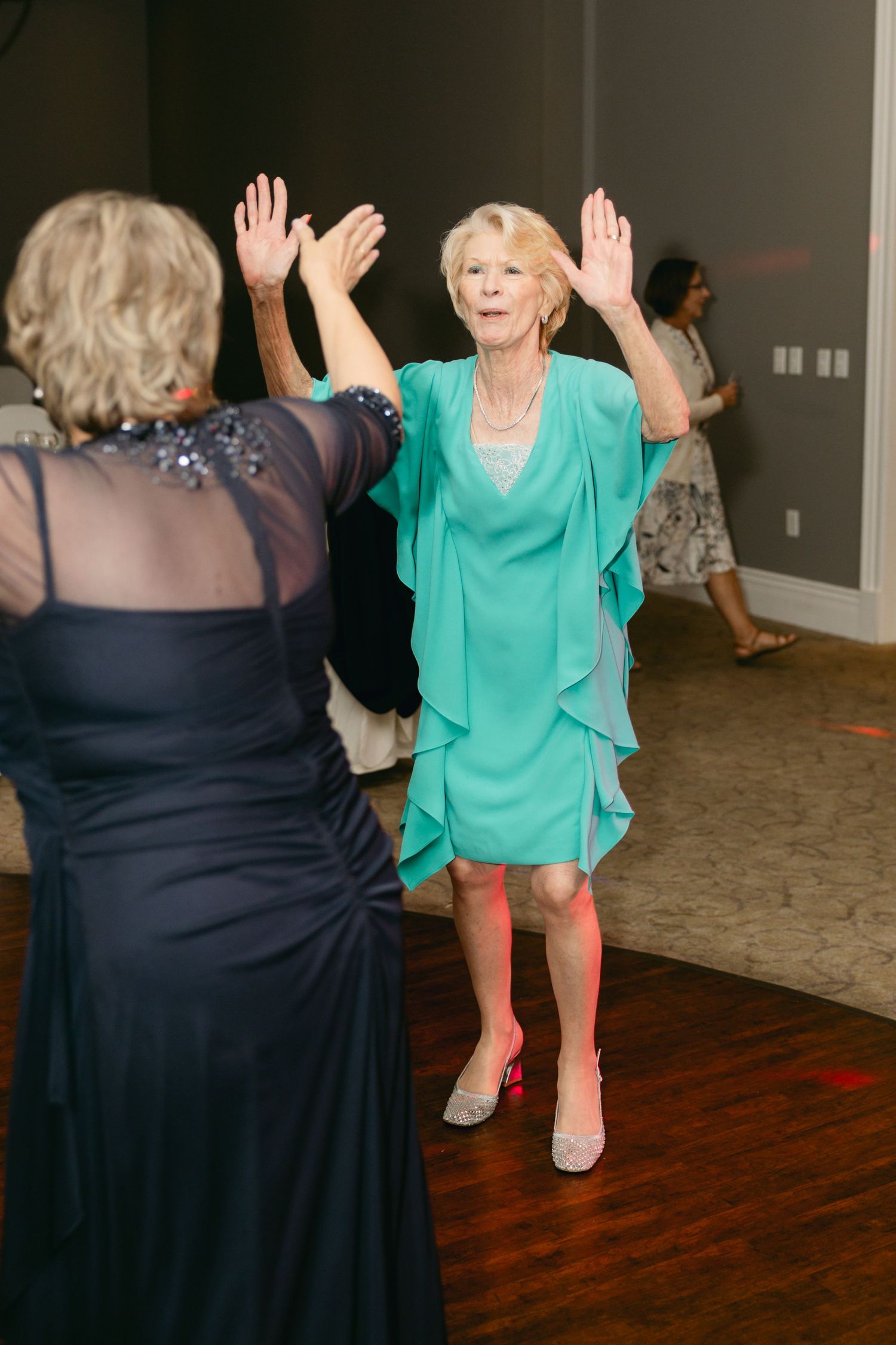 Two guests in formal attire dancing enthusiastically at wedding reception.