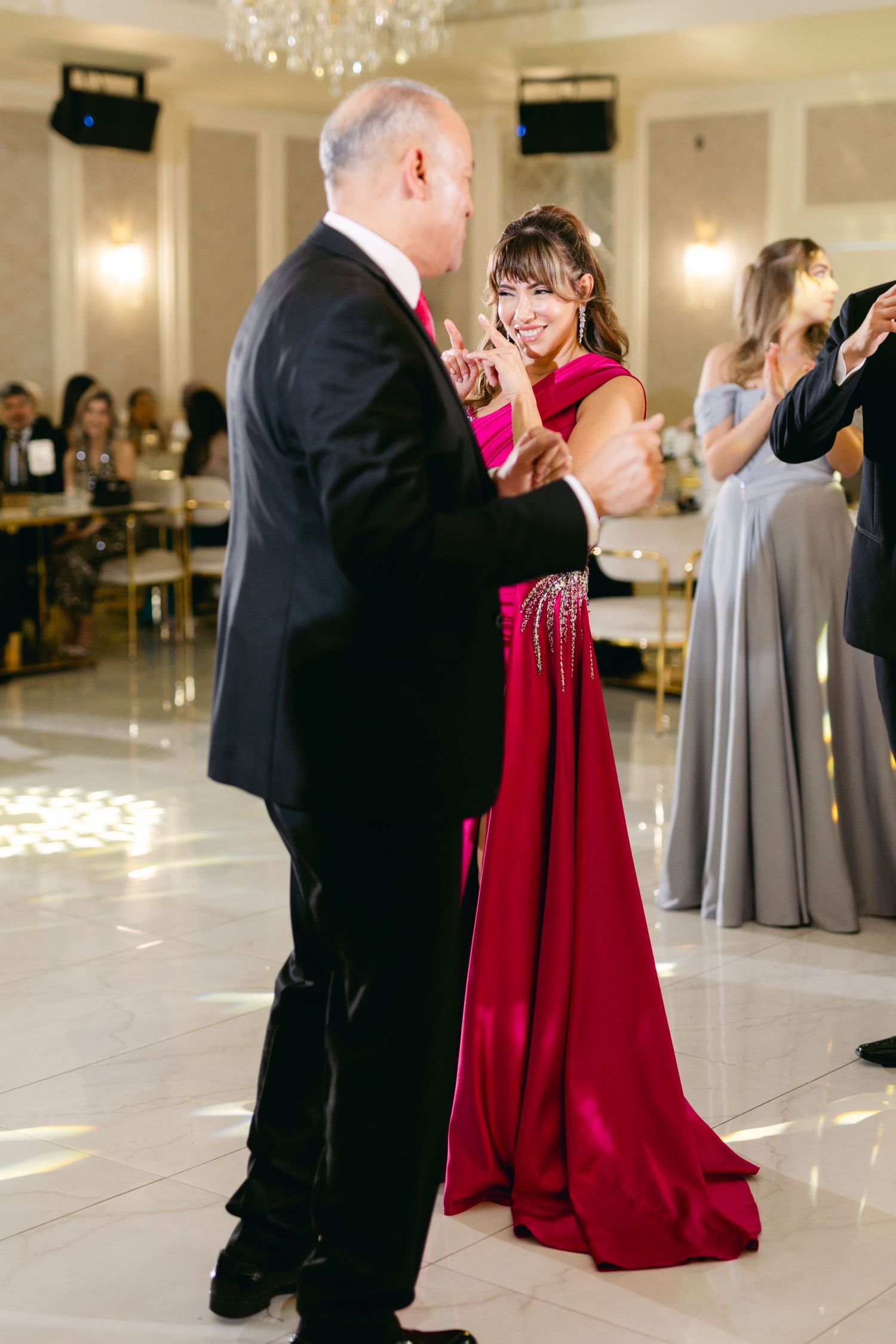 A formal dance between guests at an elegant wedding reception with chandeliers overhead.