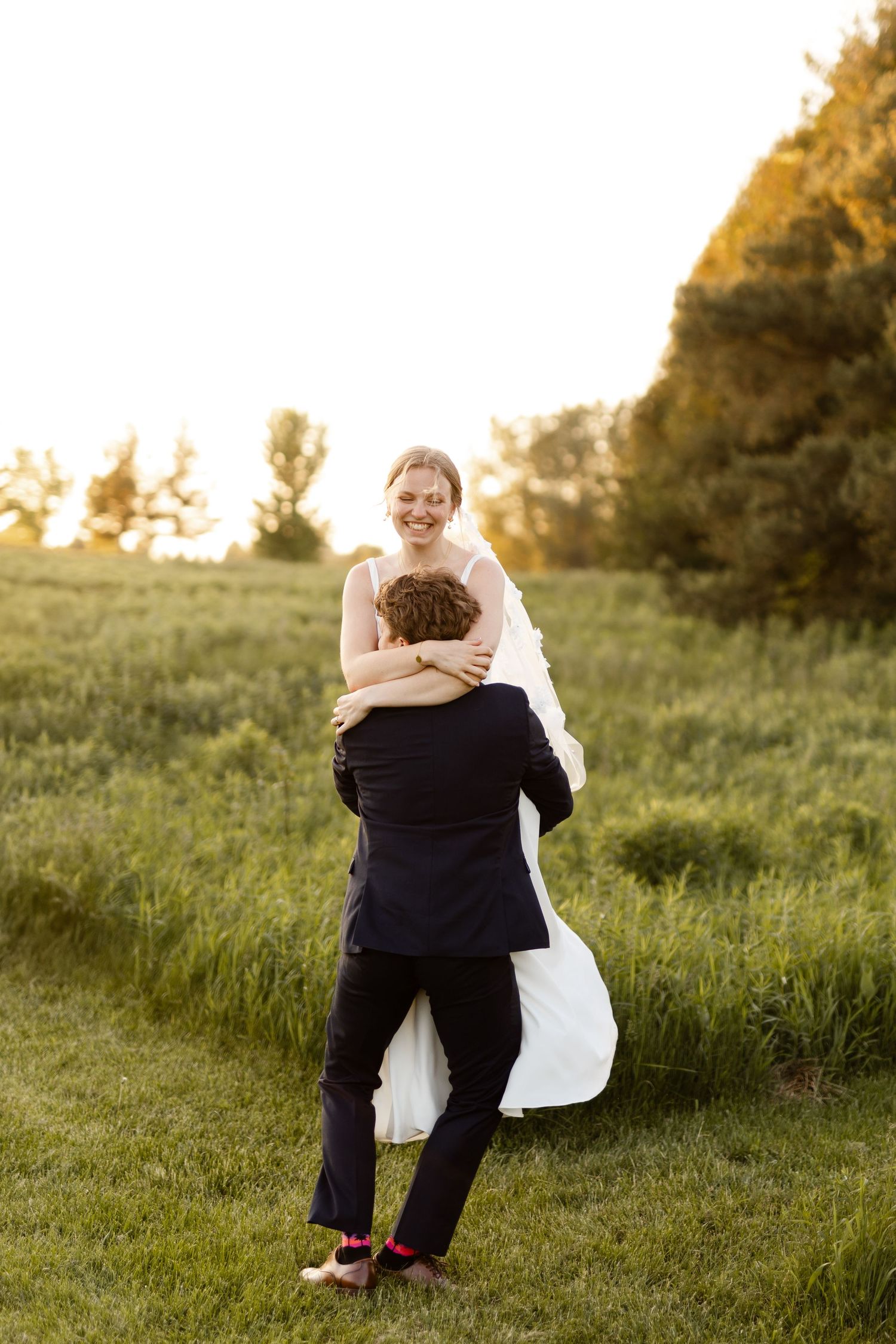 Joyful wedding embrace captured in a sun-drenched meadow.