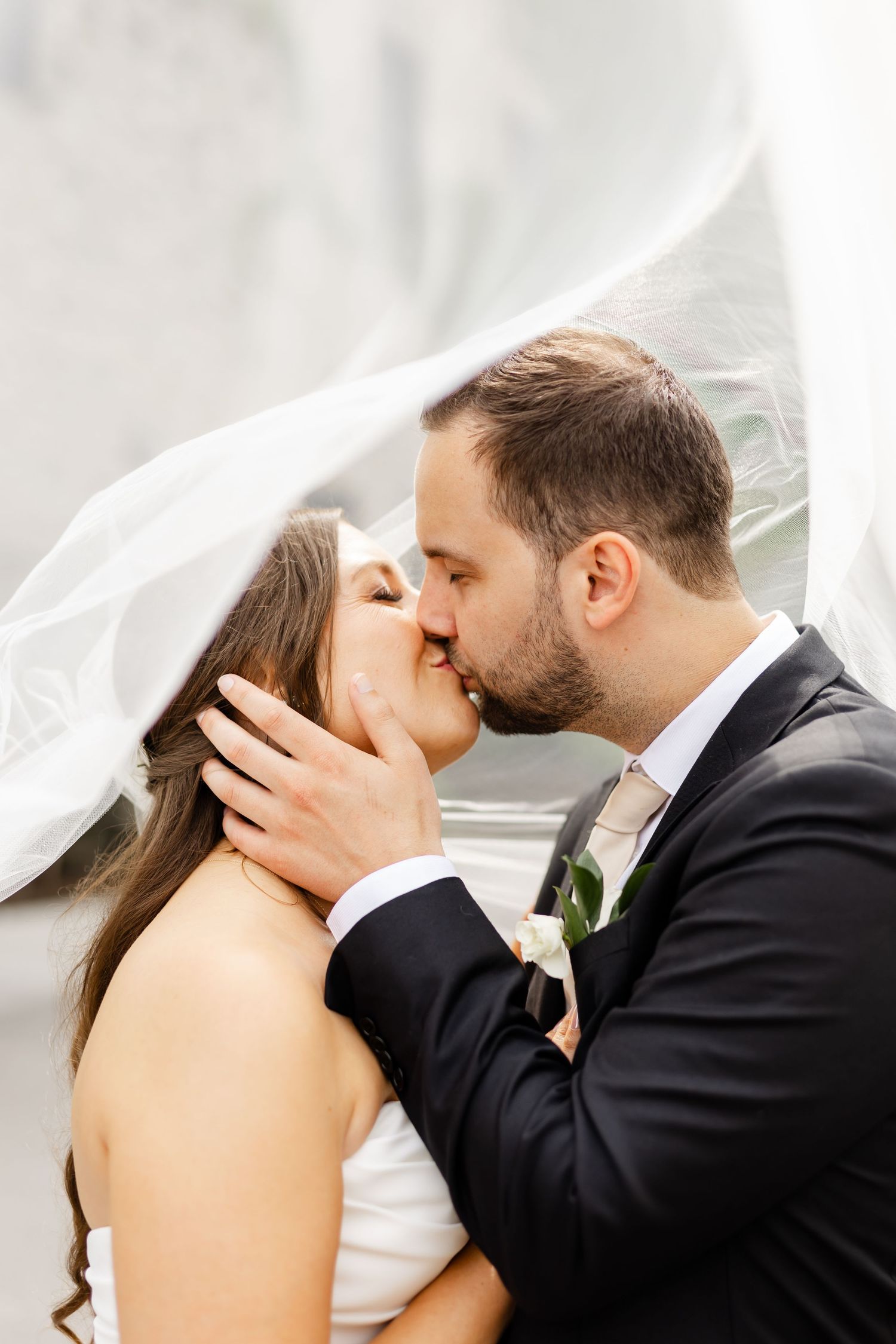 Newlyweds share a passionate kiss under the bride's flowing white veil on their wedding day.