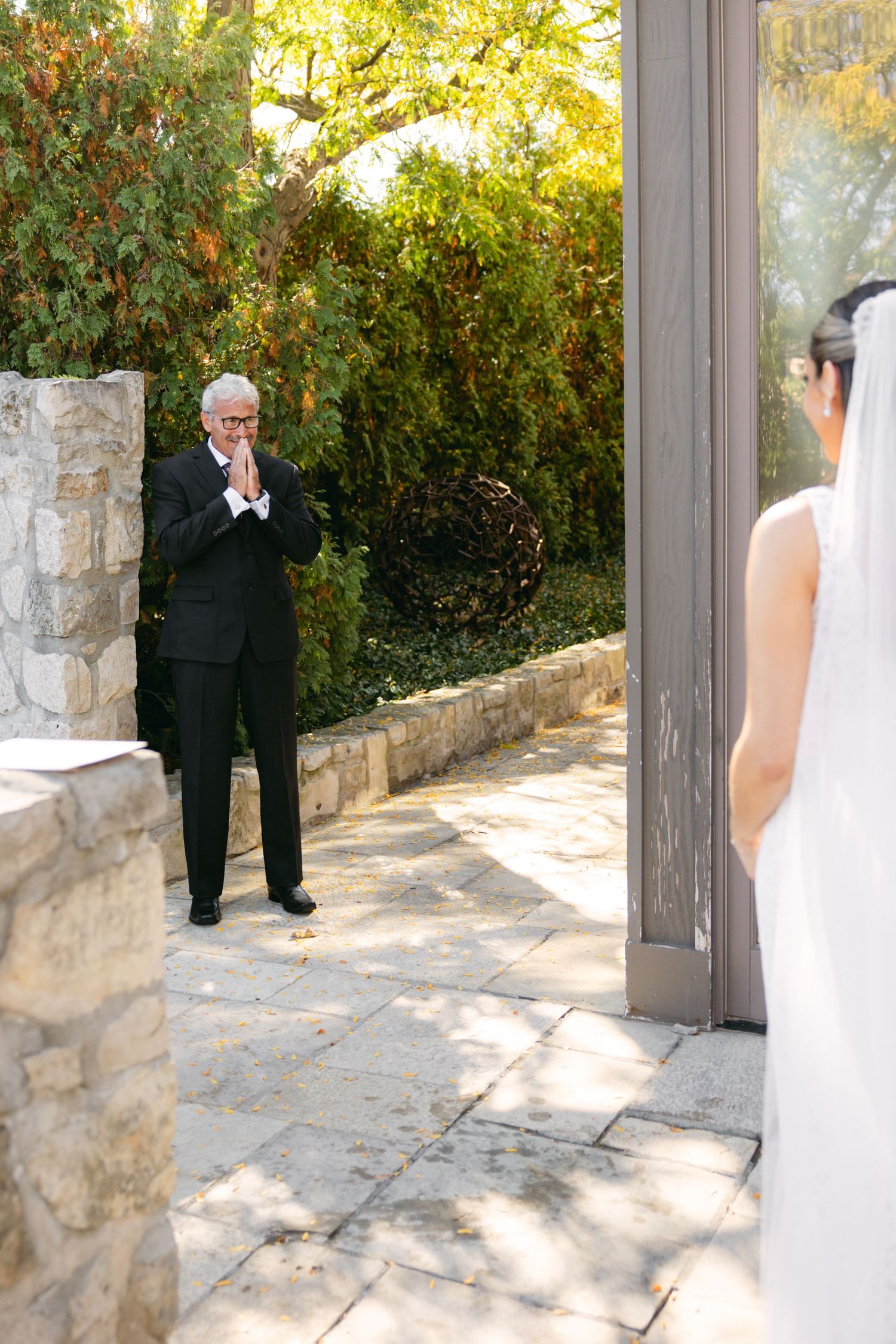 A first look wedding moment captured in a garden setting with stone walls.