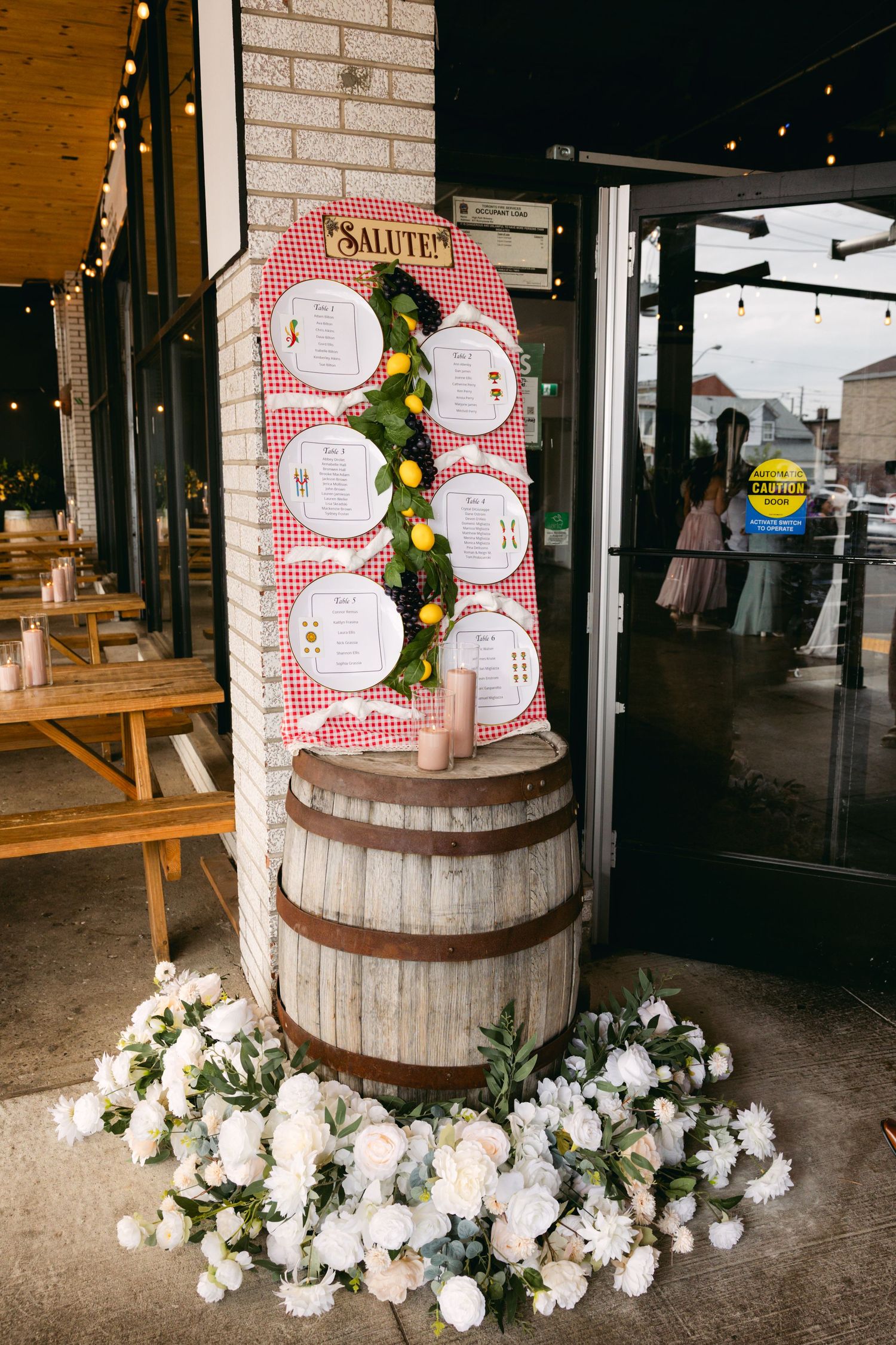 Rustic barrel display decorated with white flowers and red checkered pattern seating charts.