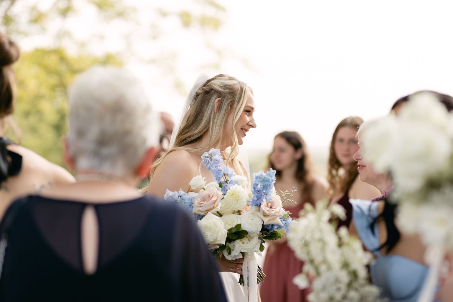 Candid moment of bride with bouquet surrounded by wedding guests outdoors.