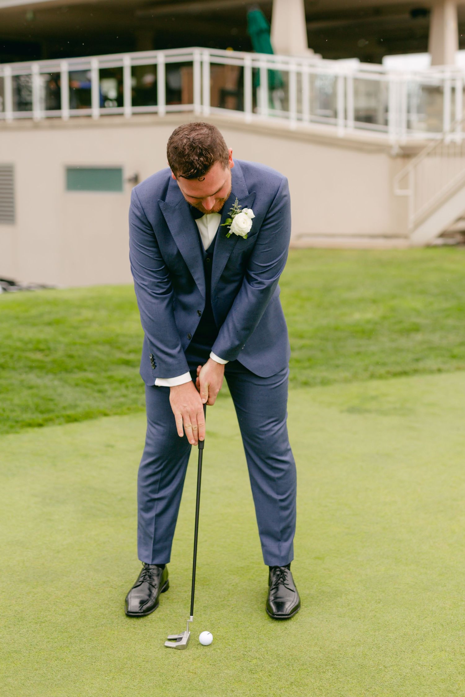 Person in blue suit lines up a golf putt on manicured green near clubhouse.