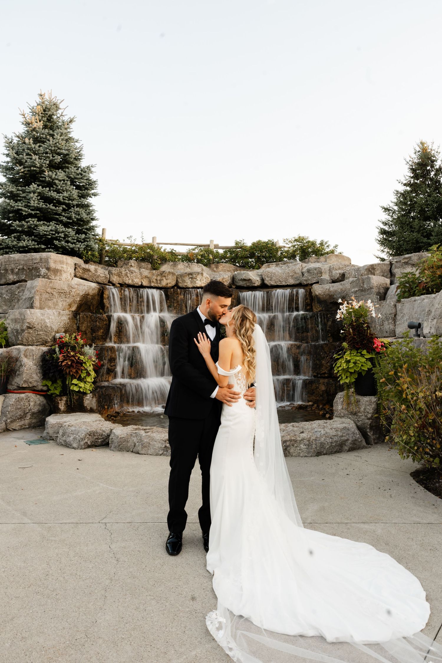 Wedding couple poses in front of a cascading stone waterfall feature.