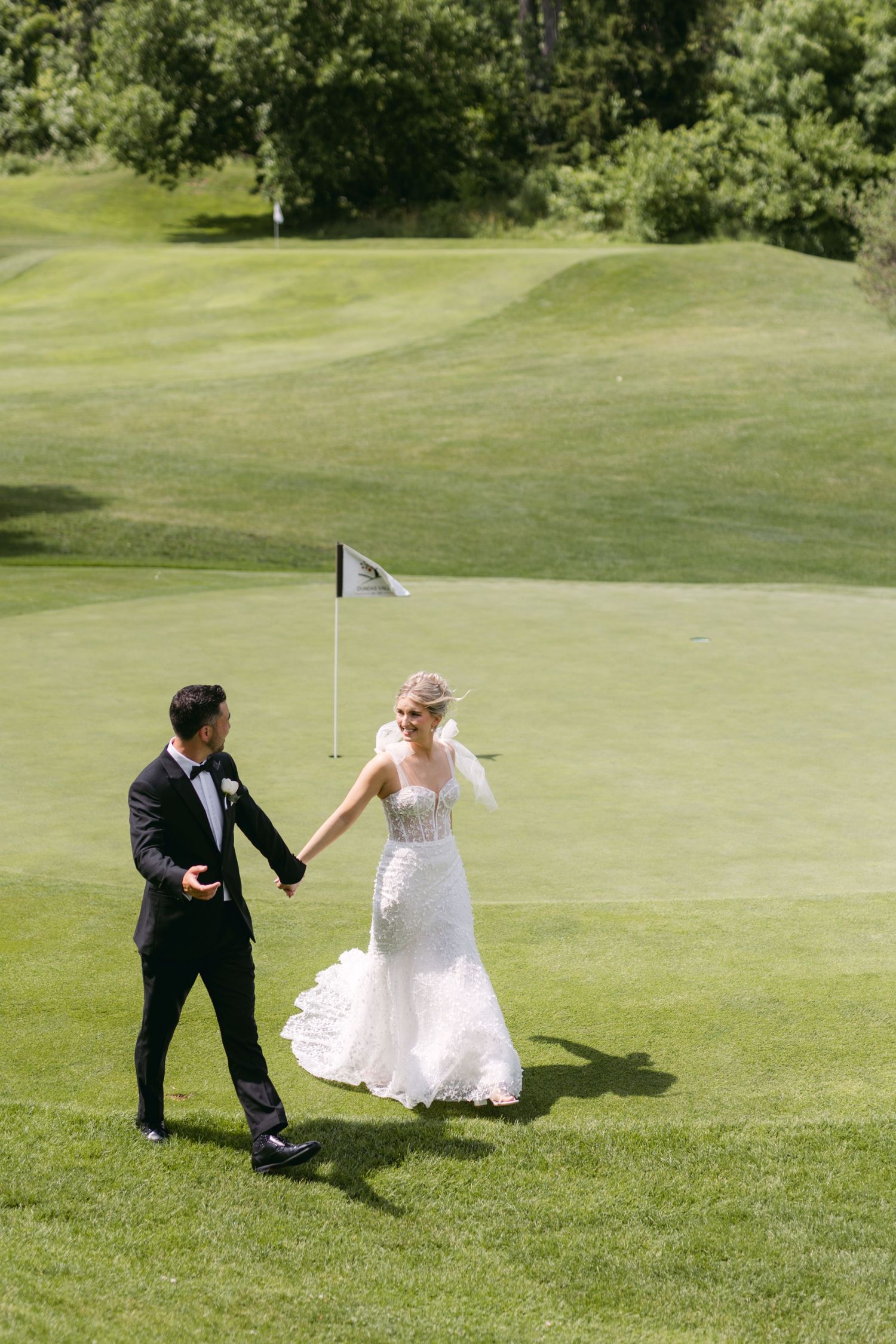 Newlyweds walking hand in hand on a golf course green with a flag in the background.