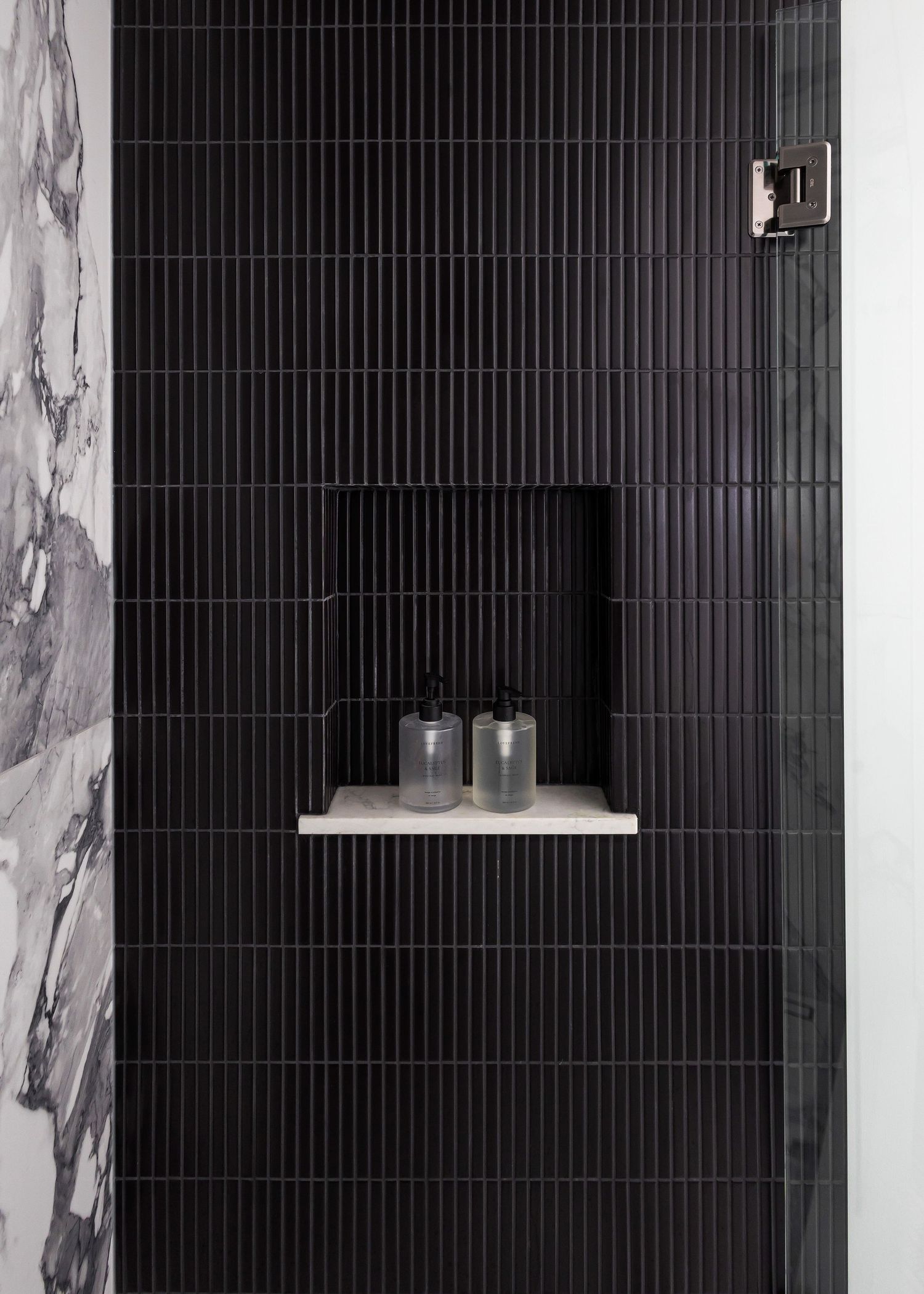 Sleek black vertical tile bathroom wall with built-in shelf niche and marble accent panel.