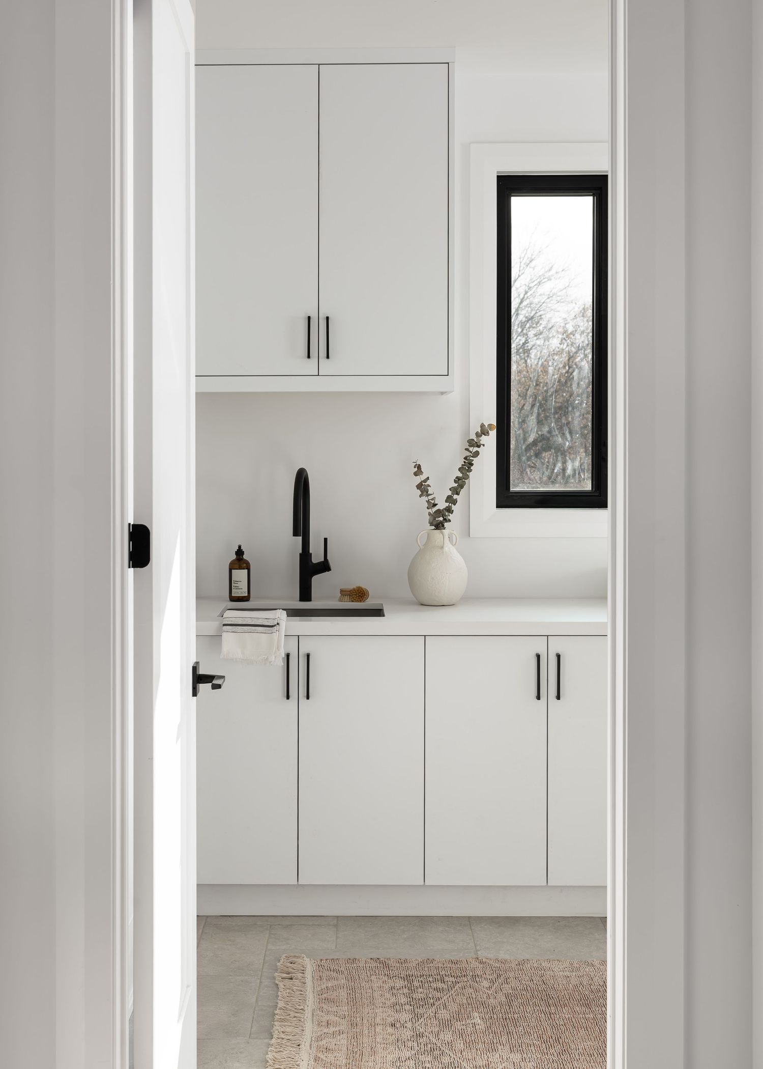 Minimalist white laundry room with black window frame and neutral runner rug.