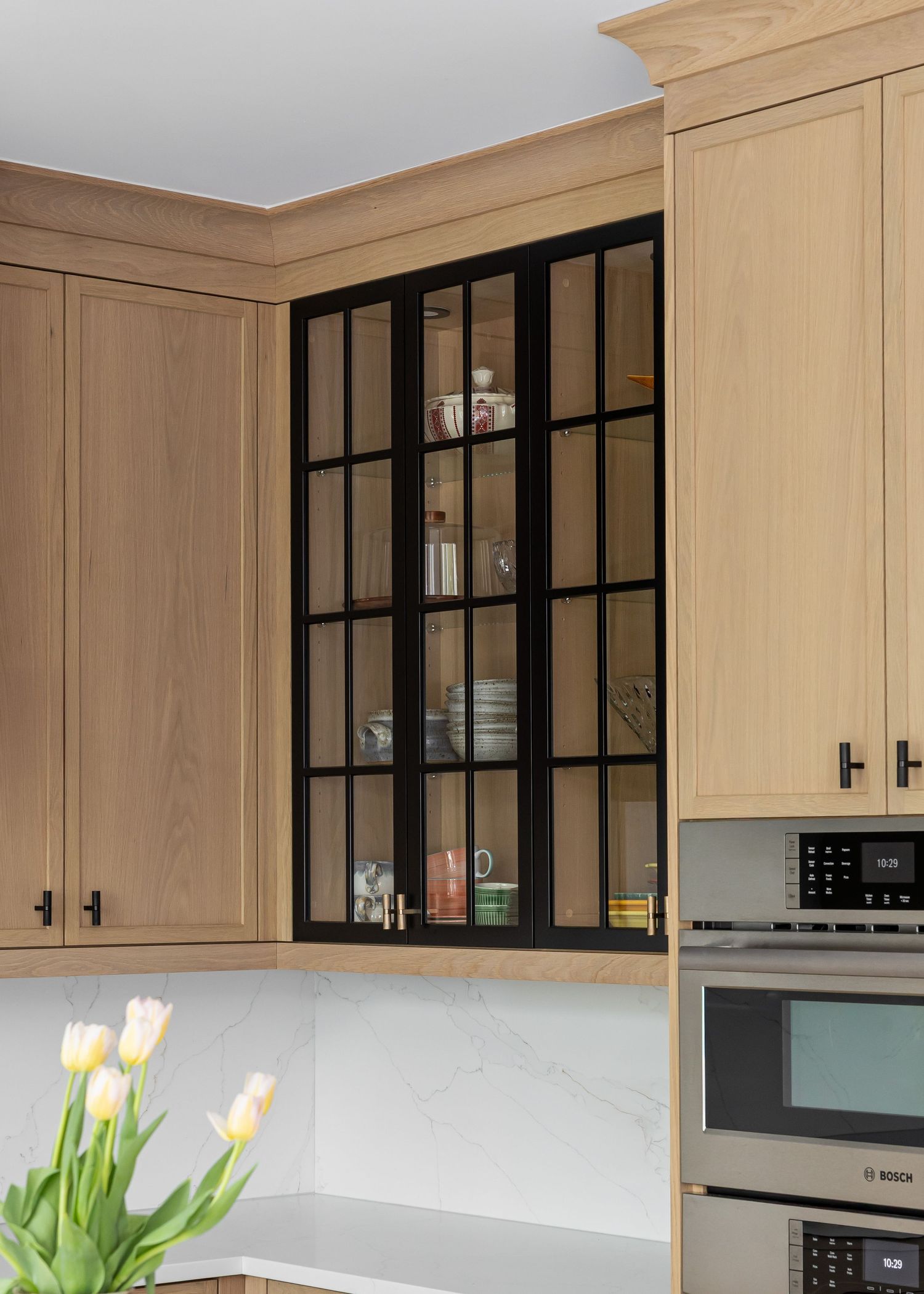Kitchen with glass-front upper cabinets, light wood finishes, and fresh tulips on display.