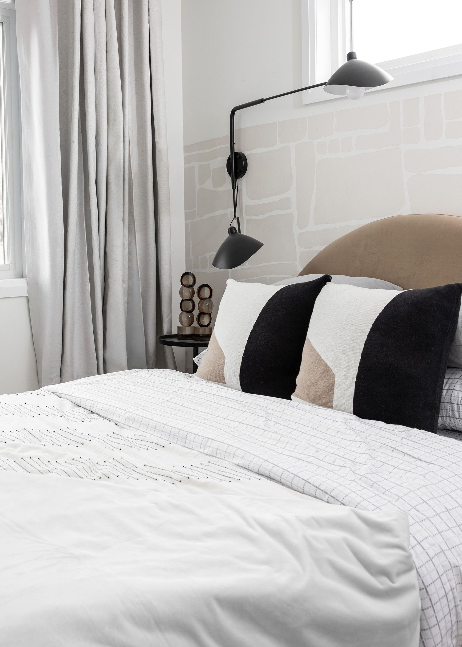 Contemporary bedroom with white linens, black accent pillows, and wall-mounted reading lights.