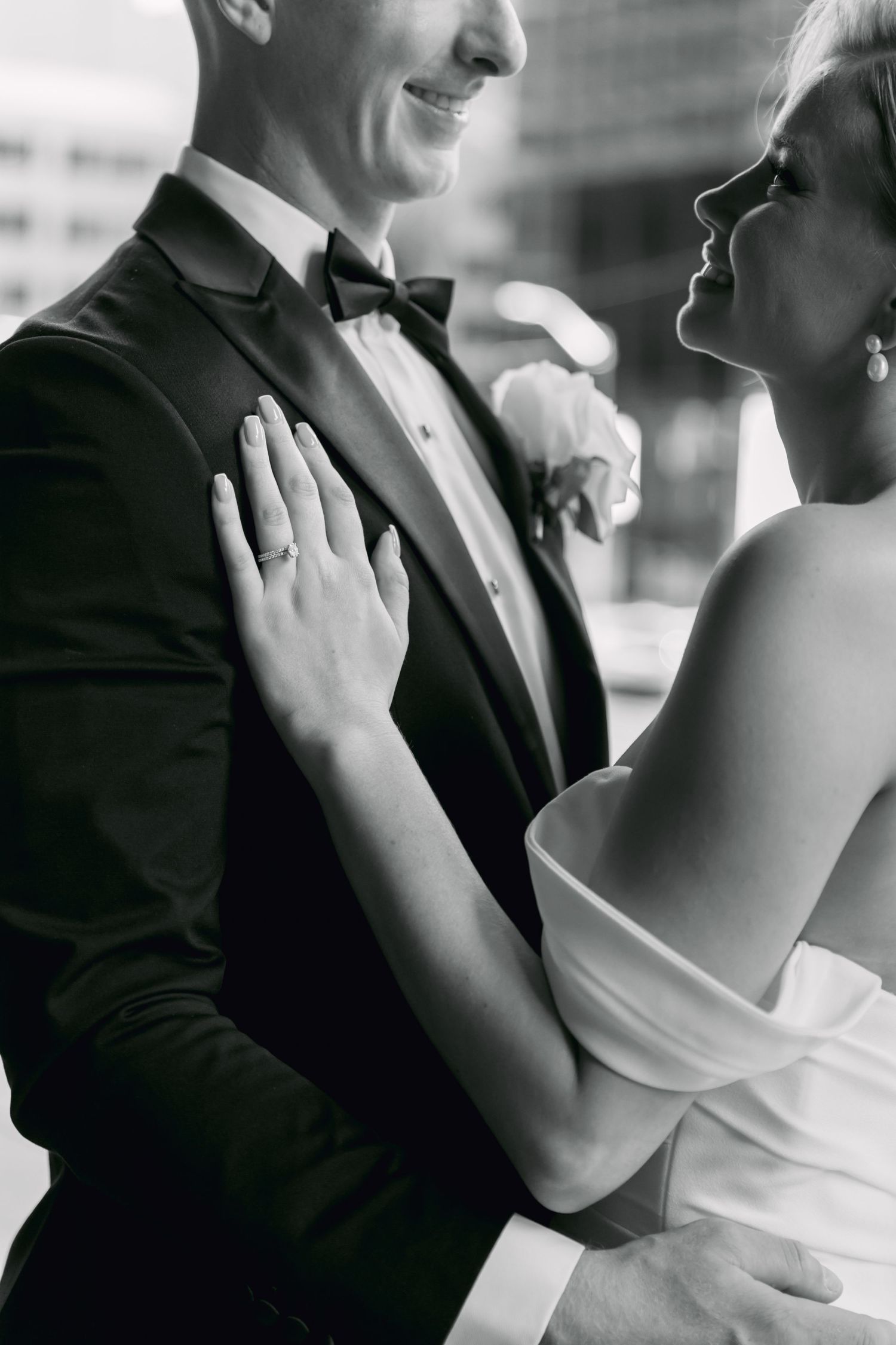 Black and white close-up of smiling bride placing hand on grooms chest, showing wedding ring.