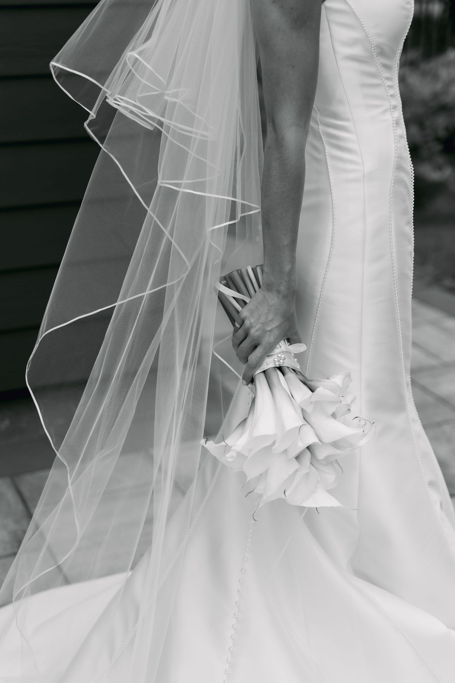 Black and white close-up of bride holding white calla lily bouquet with flowing veil cascading down.