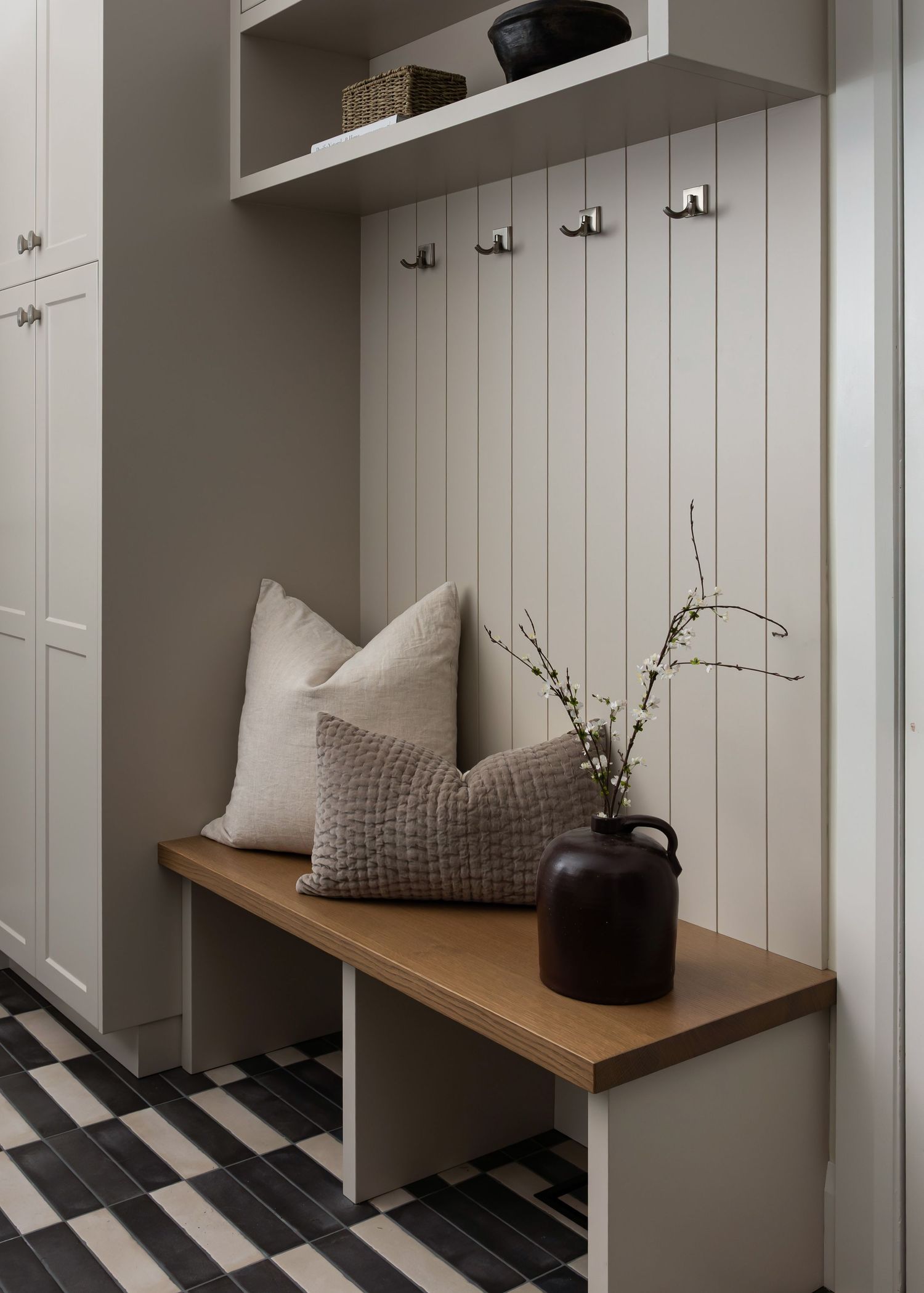 Modern mudroom with white paneled walls, wooden bench, and black and white checkered floor.