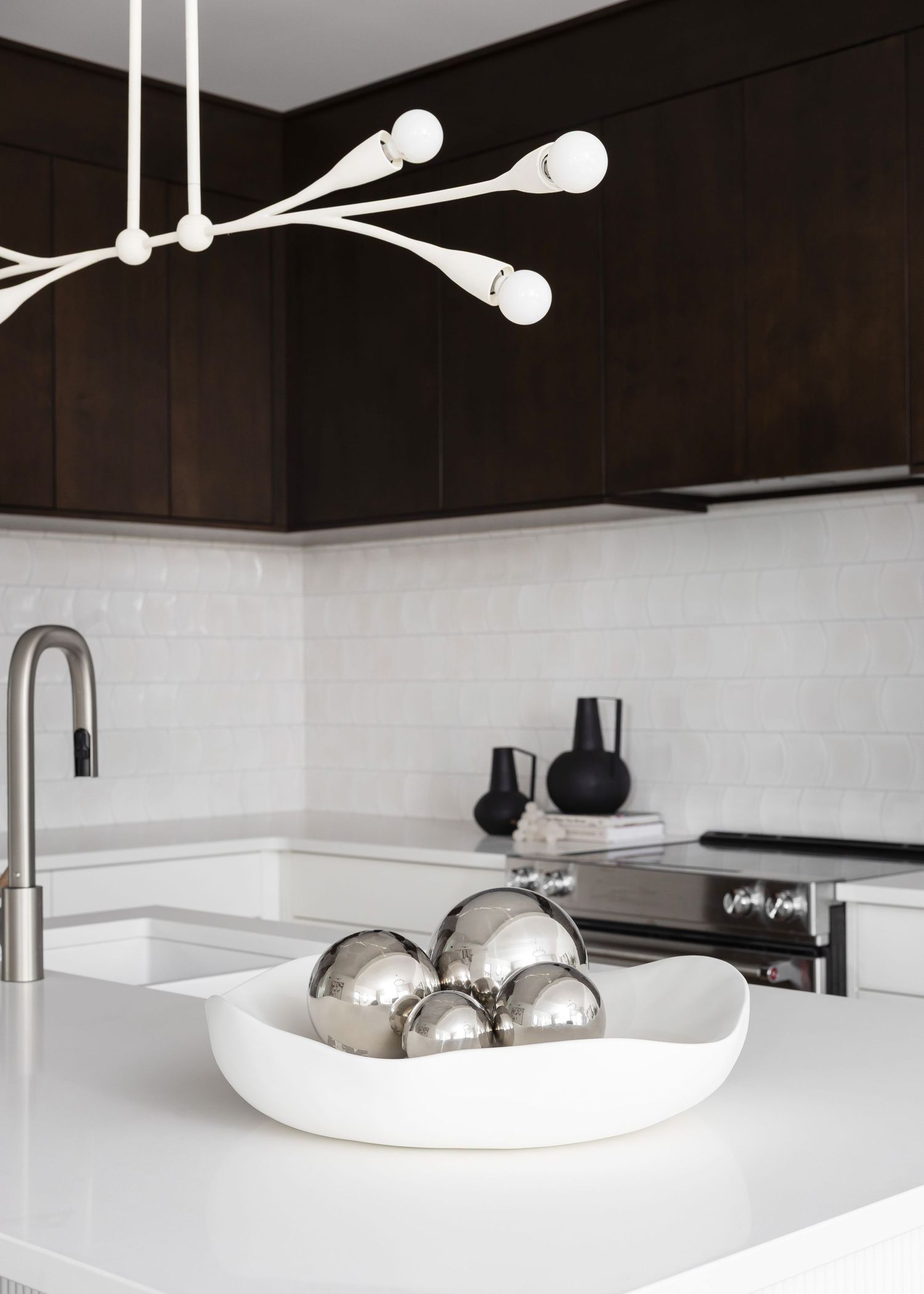 Contemporary kitchen with white countertops, dark cabinets and modern pendant lighting.