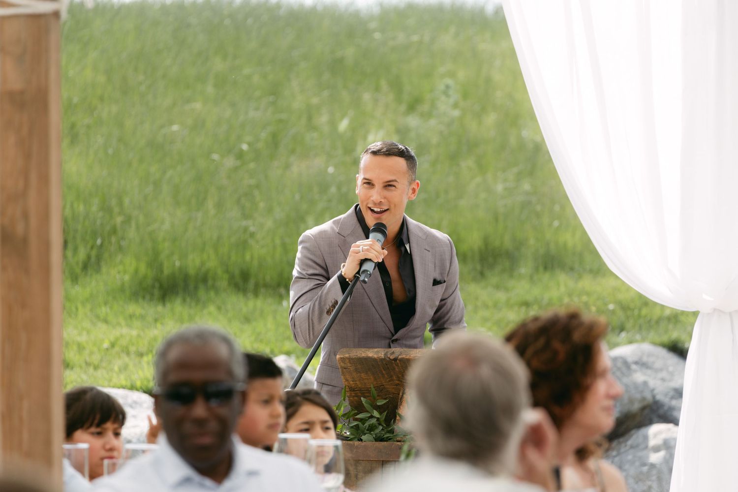 A speaker addresses wedding guests during an outdoor reception ceremony.