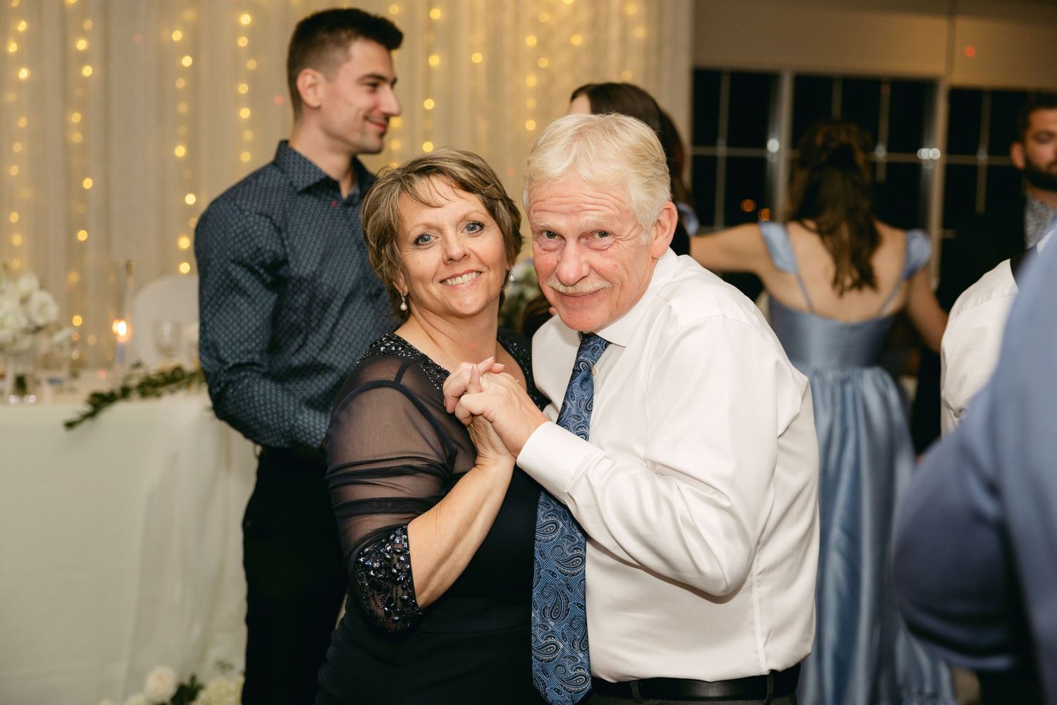 Couples dancing together at an evening wedding reception with twinkle lights in background.