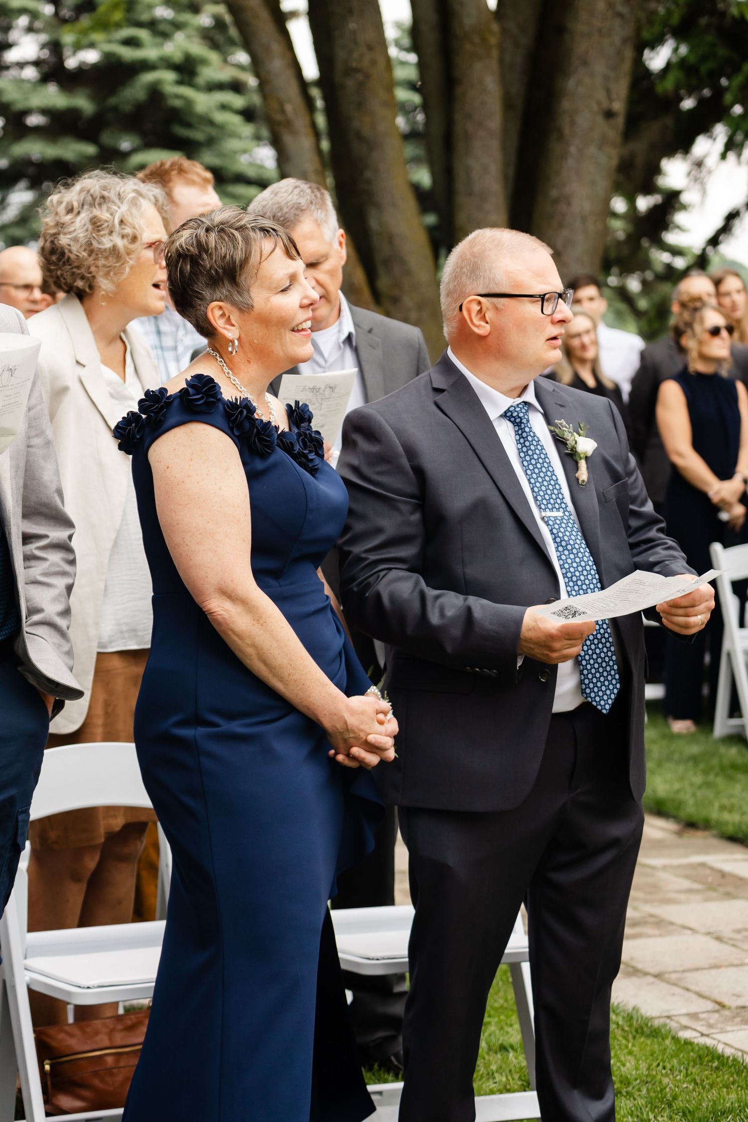 Wedding guests in formal attire participating in outdoor ceremony.