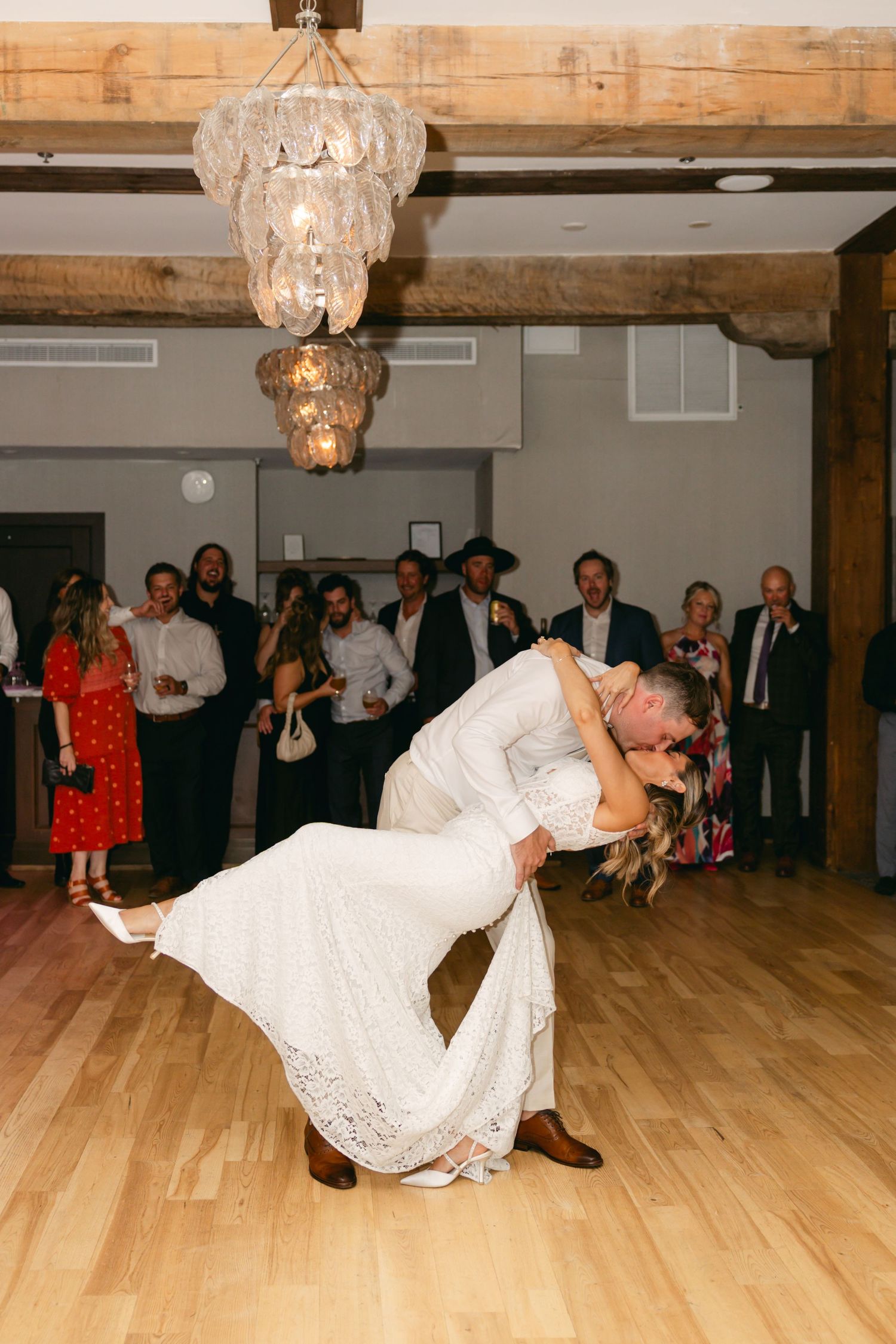 A couple performs an energetic dance dip on a wooden floor during a wedding reception.