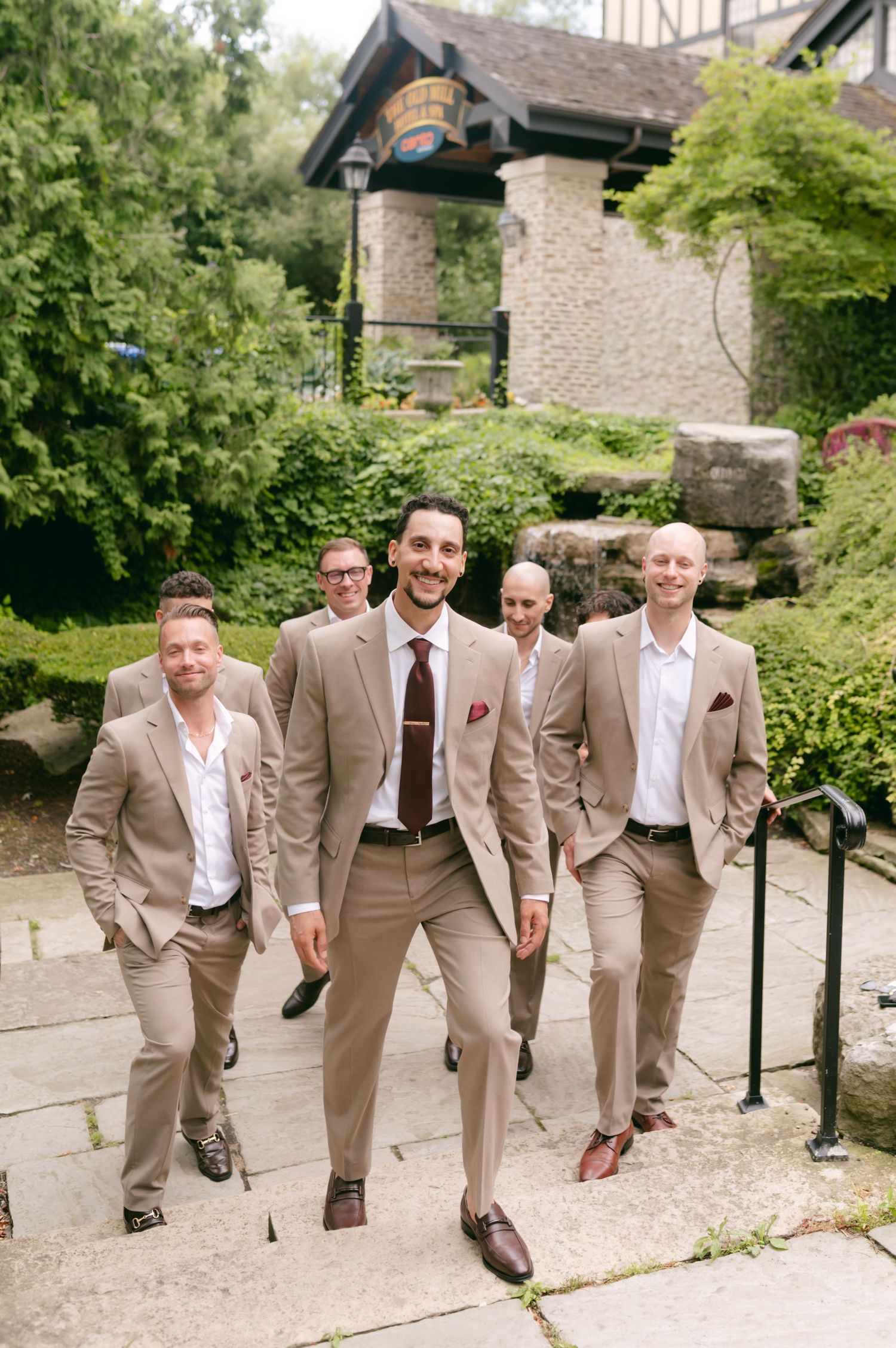 Wedding party in khaki suits walking together on a stone pathway.