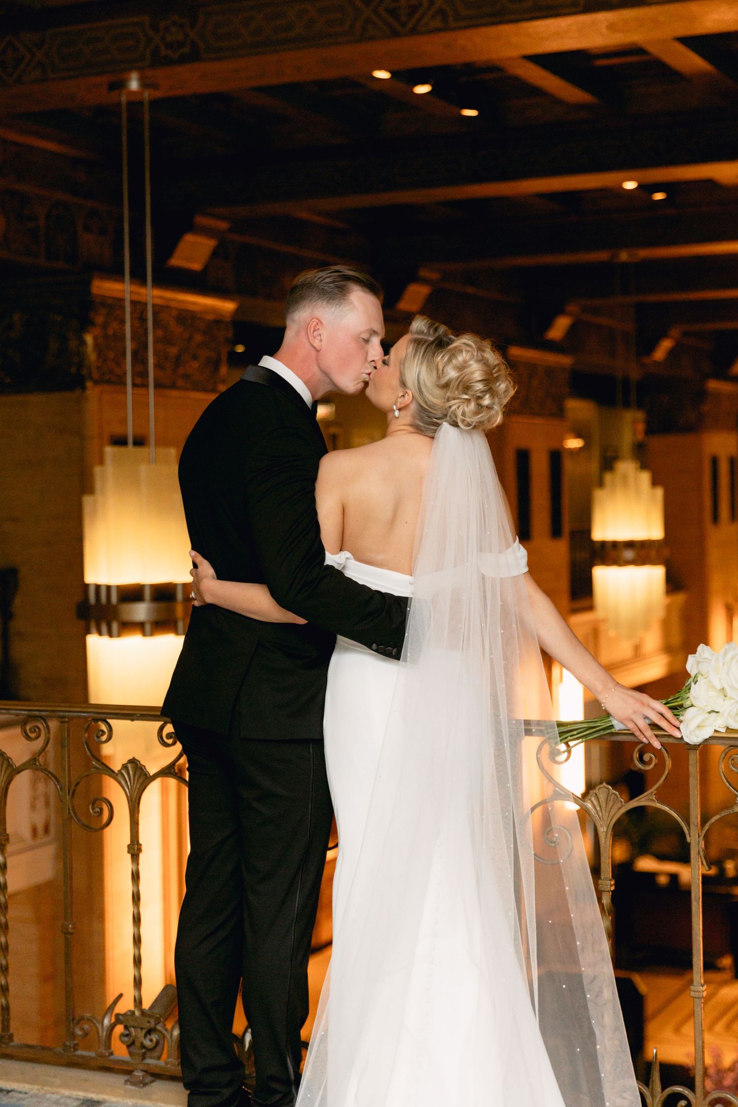 Bride and groom share a romantic first kiss at elegant indoor wedding venue with warm ambient lighting.