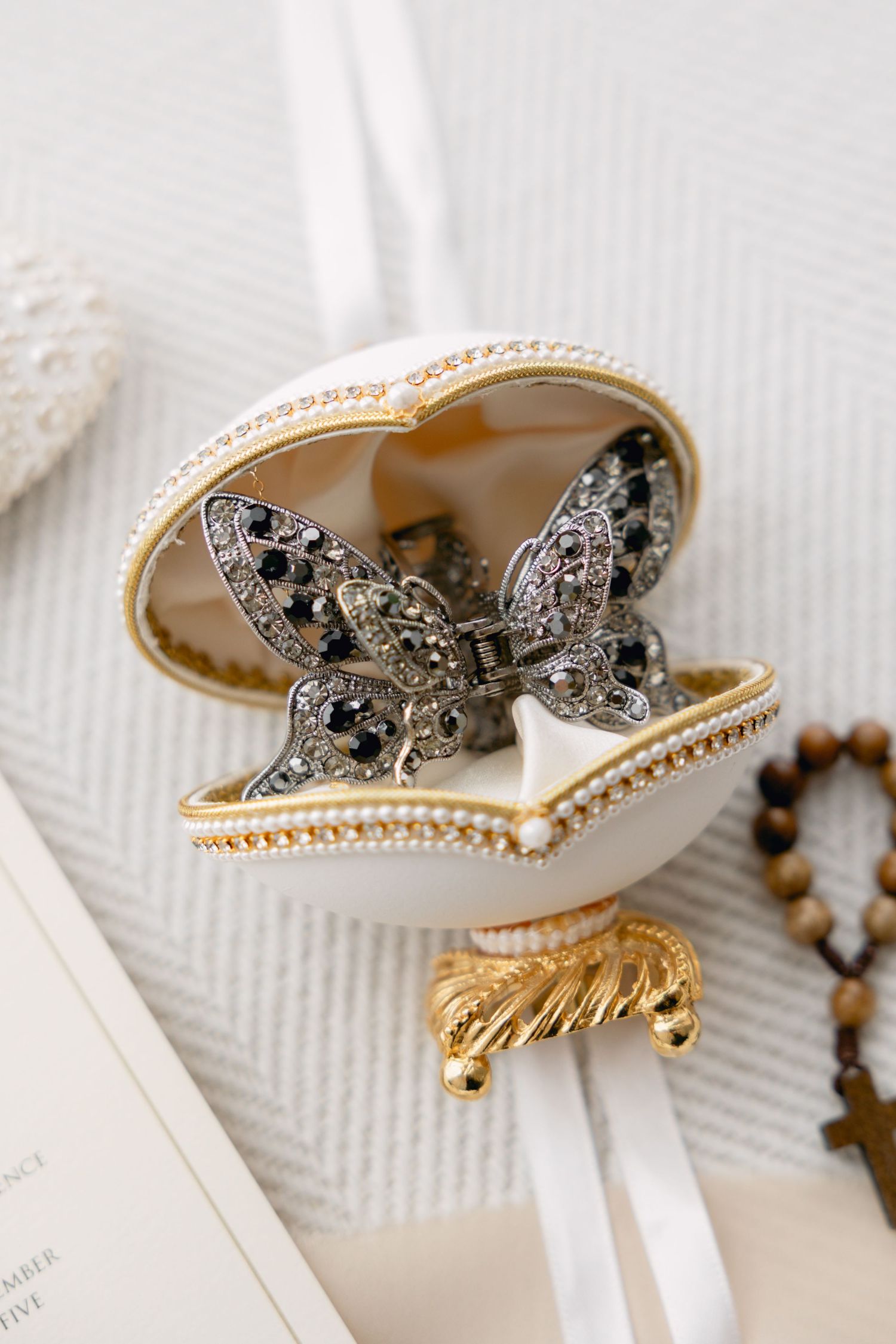 Elegant white jeweled trinket box with butterfly brooch inside, adorned with pearls and gold accents.