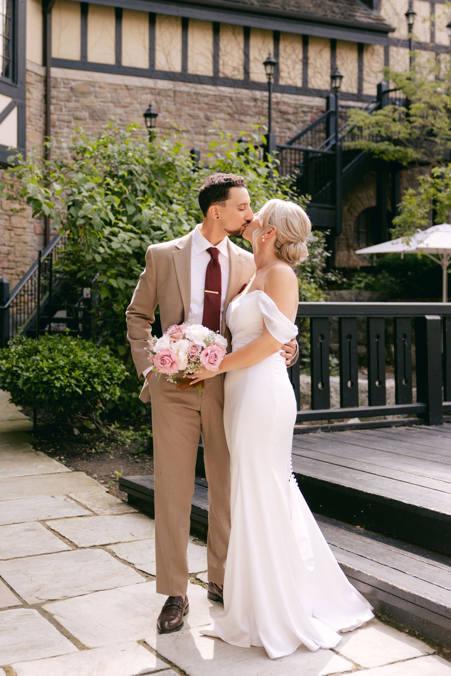 Romantic wedding moment captured on stone patio with classic architecture backdrop.