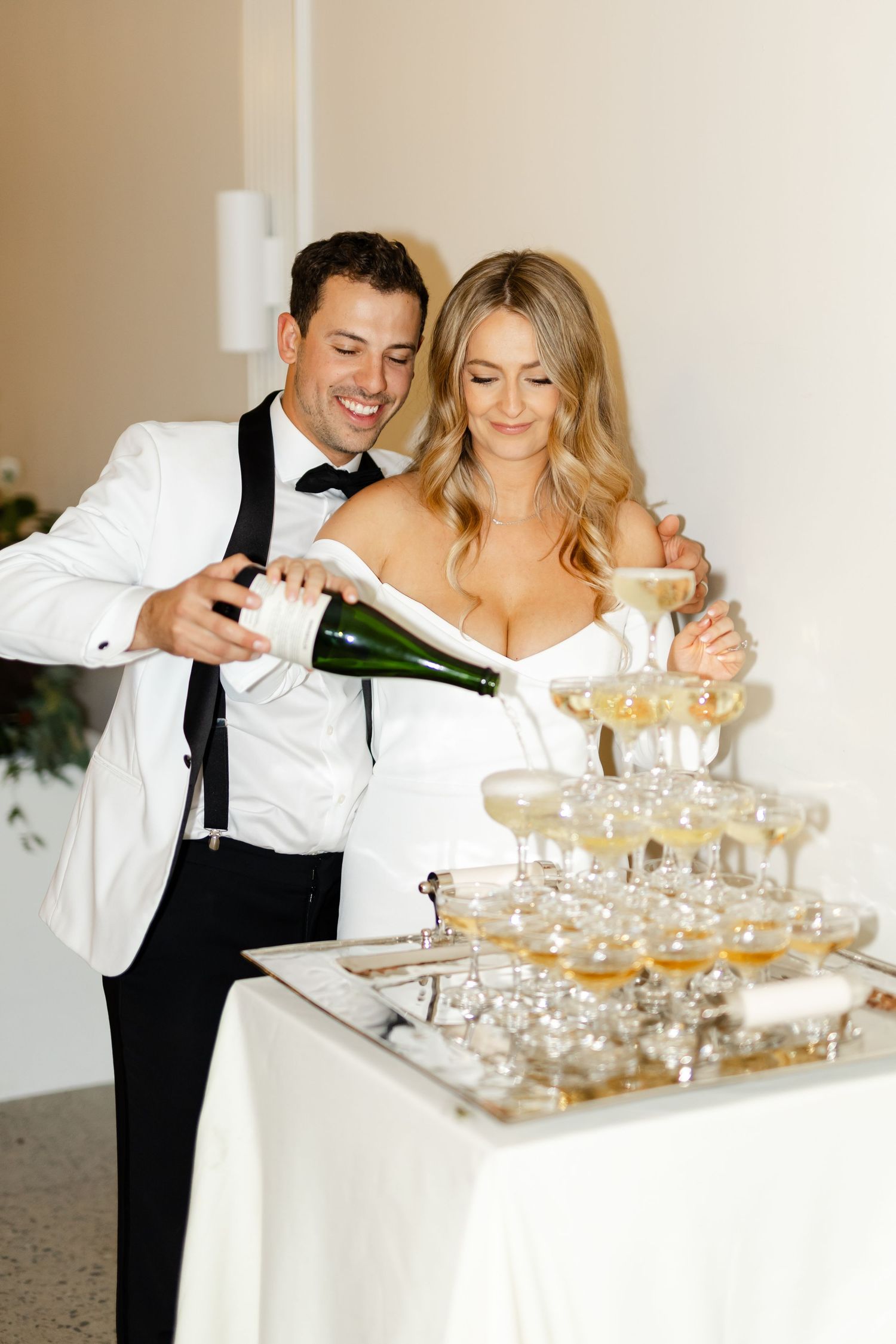 Couple in formal attire creating a champagne tower together at an elegant celebration.