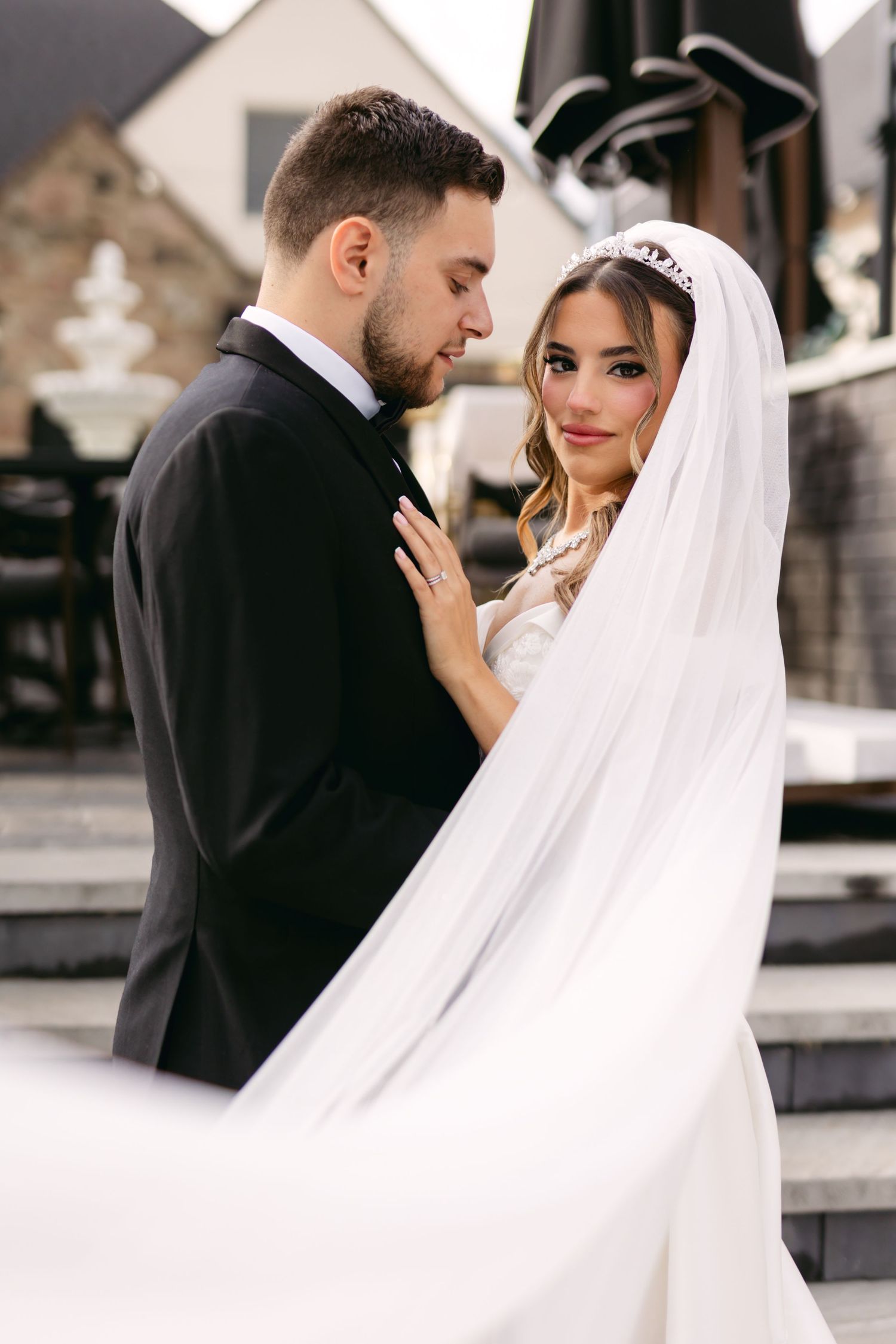 Intimate wedding portrait with flowing cathedral veil against stone architecture.
