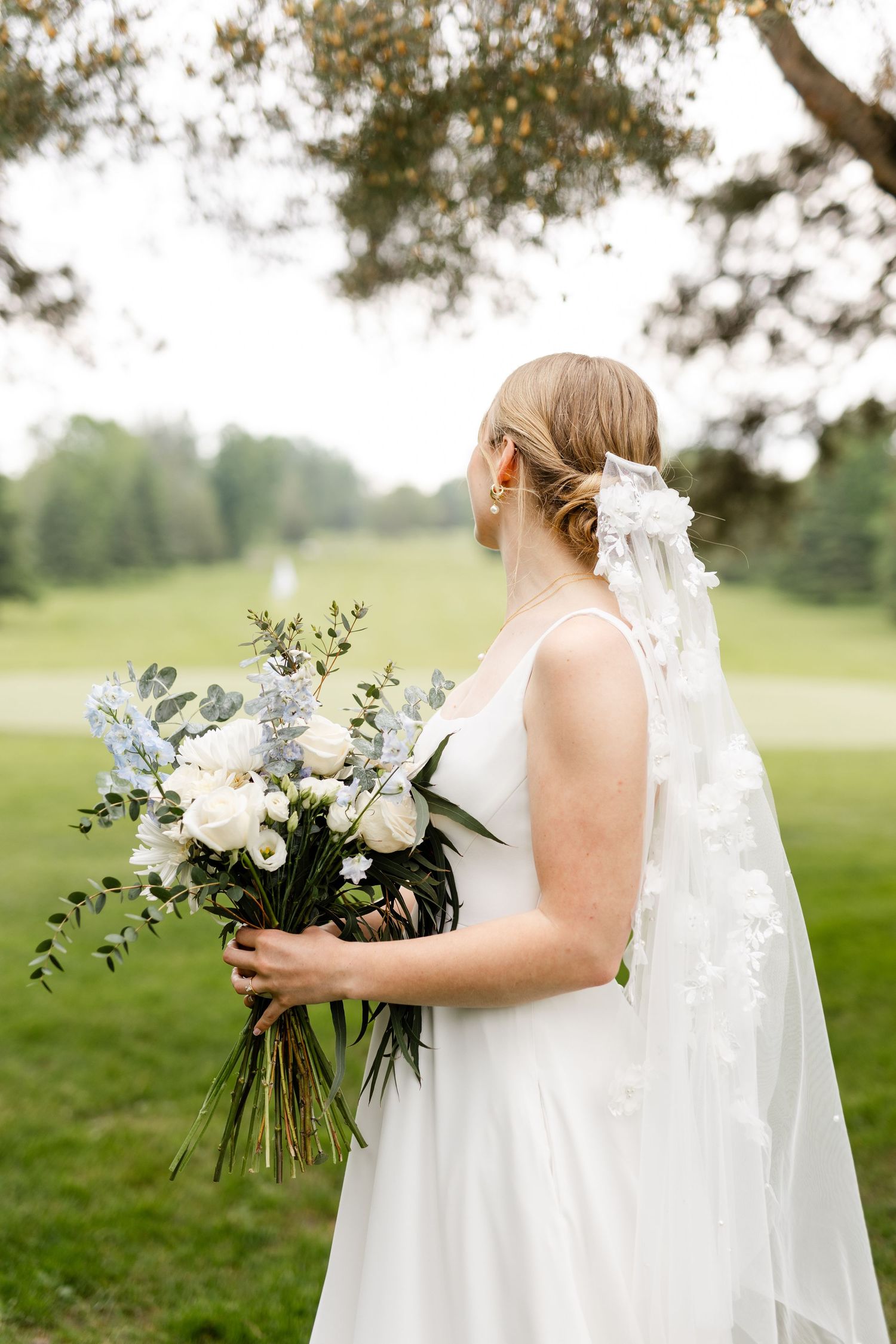 Side profile of bride holding elegant white and blue bouquet with flowing veil.