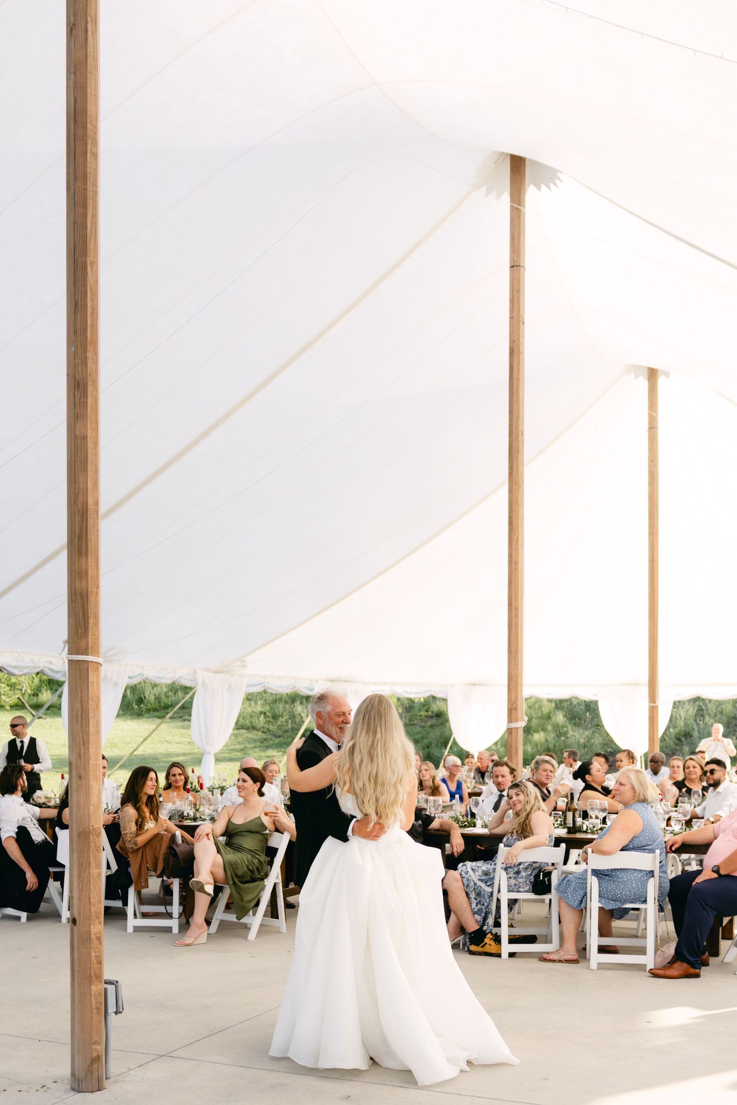 Guests gather under a bright white tent for wedding festivities.