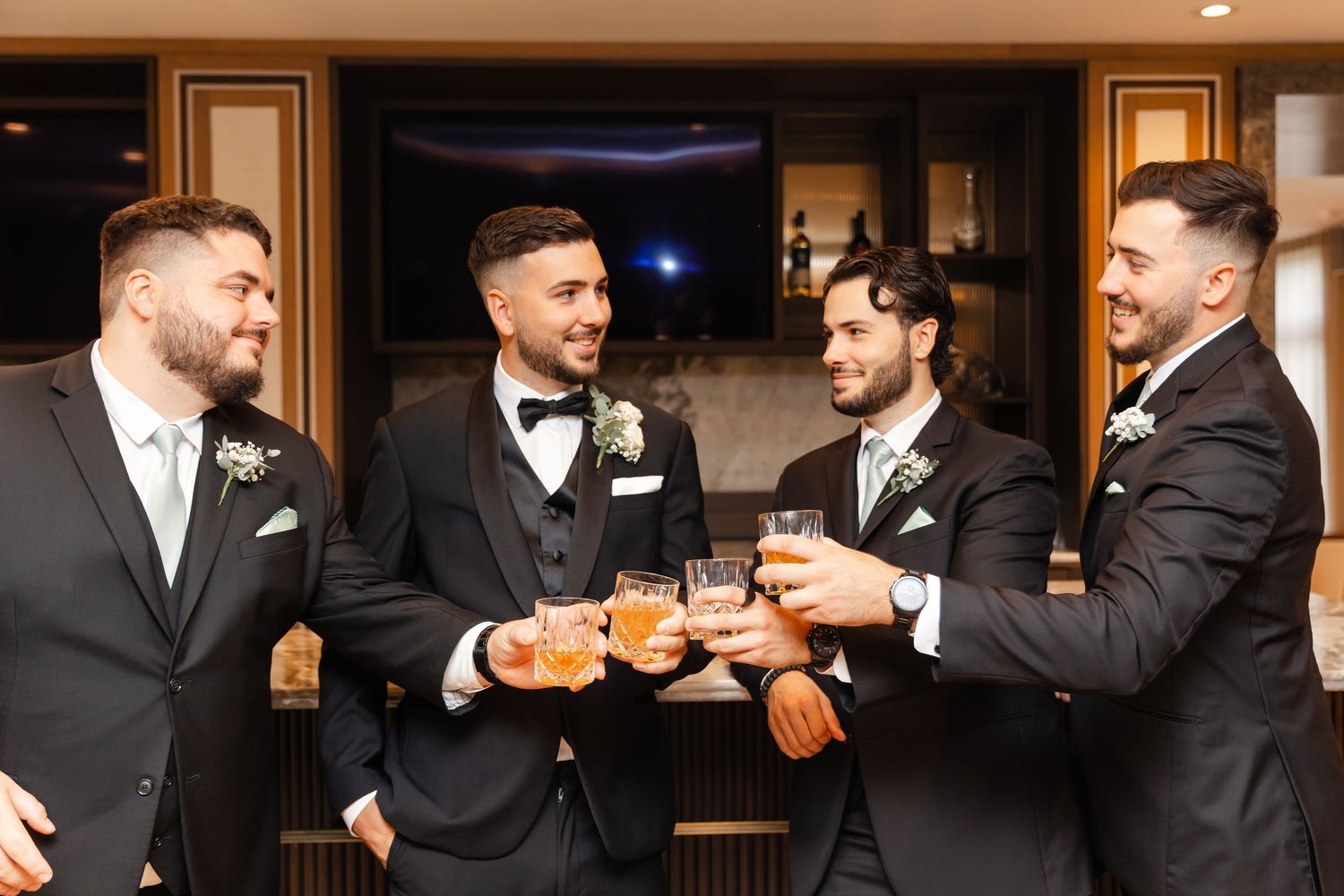 Groomsmen sharing drinks and laughing together during wedding reception.