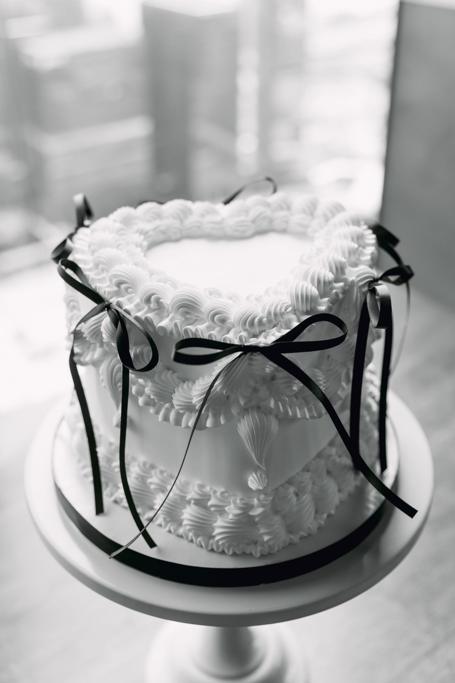 Elegant white wedding cake decorated with rosette frosting and black ribbon bows on a white cake stand.