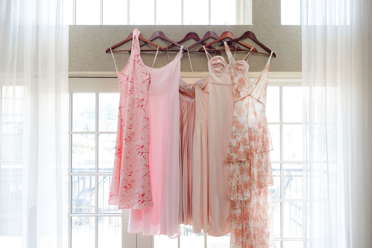 Pink and floral bridesmaid dresses hanging on display against white curtains.