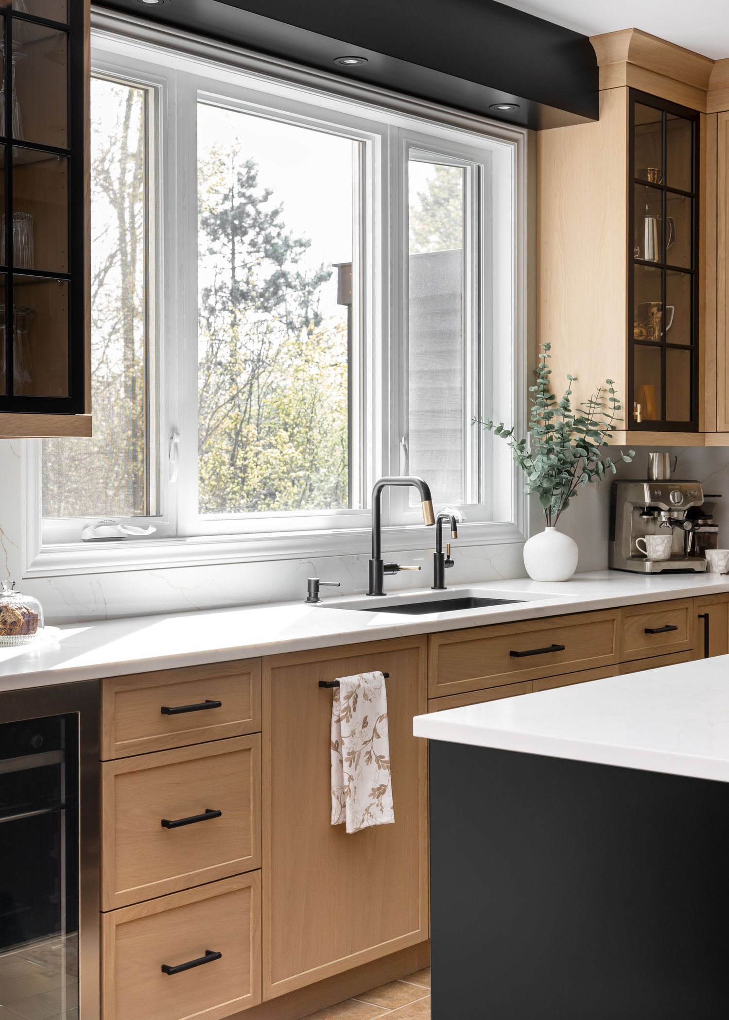 Expansive kitchen windows provide natural light over white countertops and tan cabinetry.