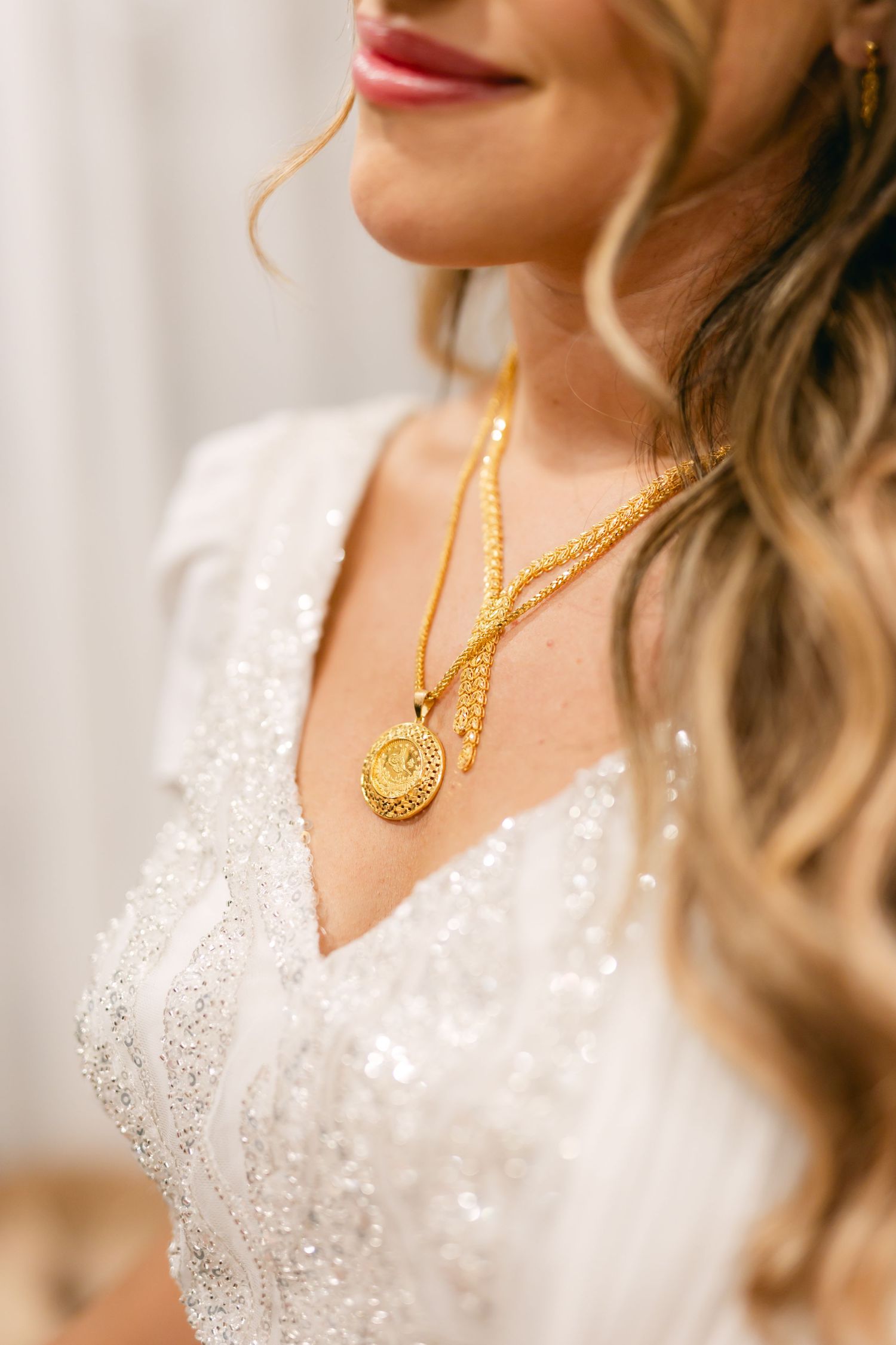 Sparkling white wedding dress with intricate beading and a gold necklace detail.