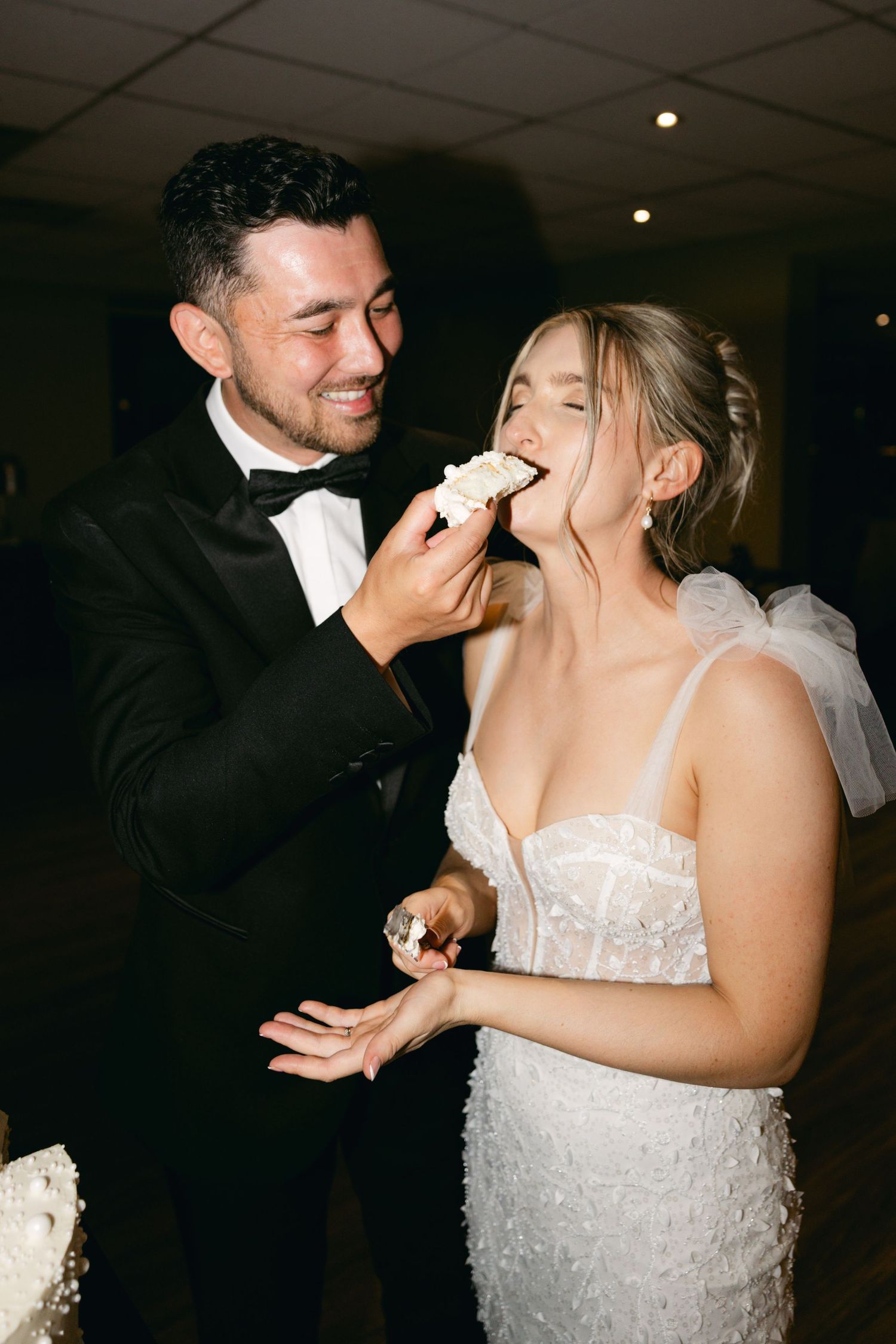 Newlywed couple shares a playful cake-feeding moment during their wedding reception celebration.
