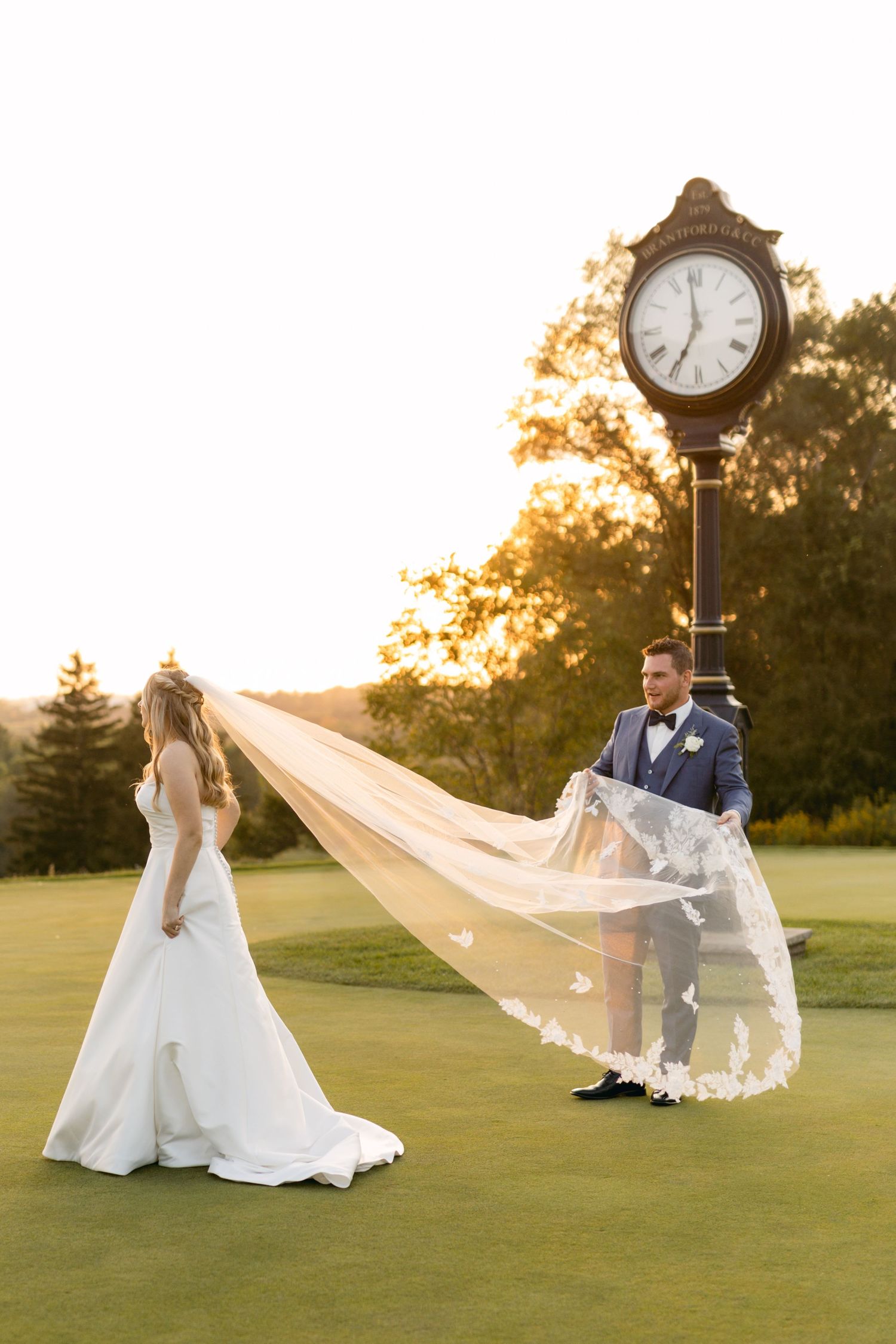 Wedding couple poses by vintage clock post on golf course during golden hour.