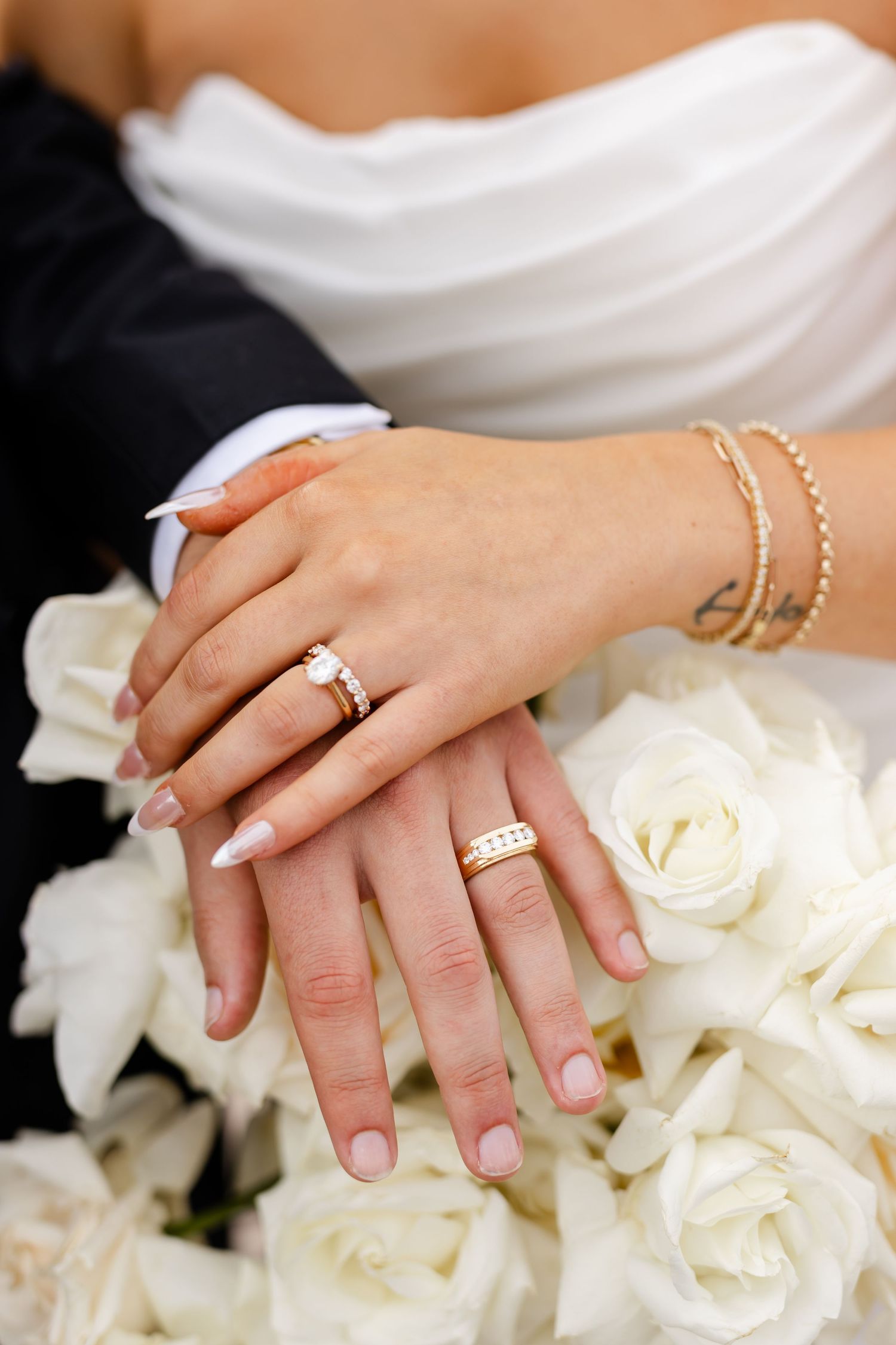 Newlyweds display wedding rings resting on white rose bridal bouquet after ceremony.
